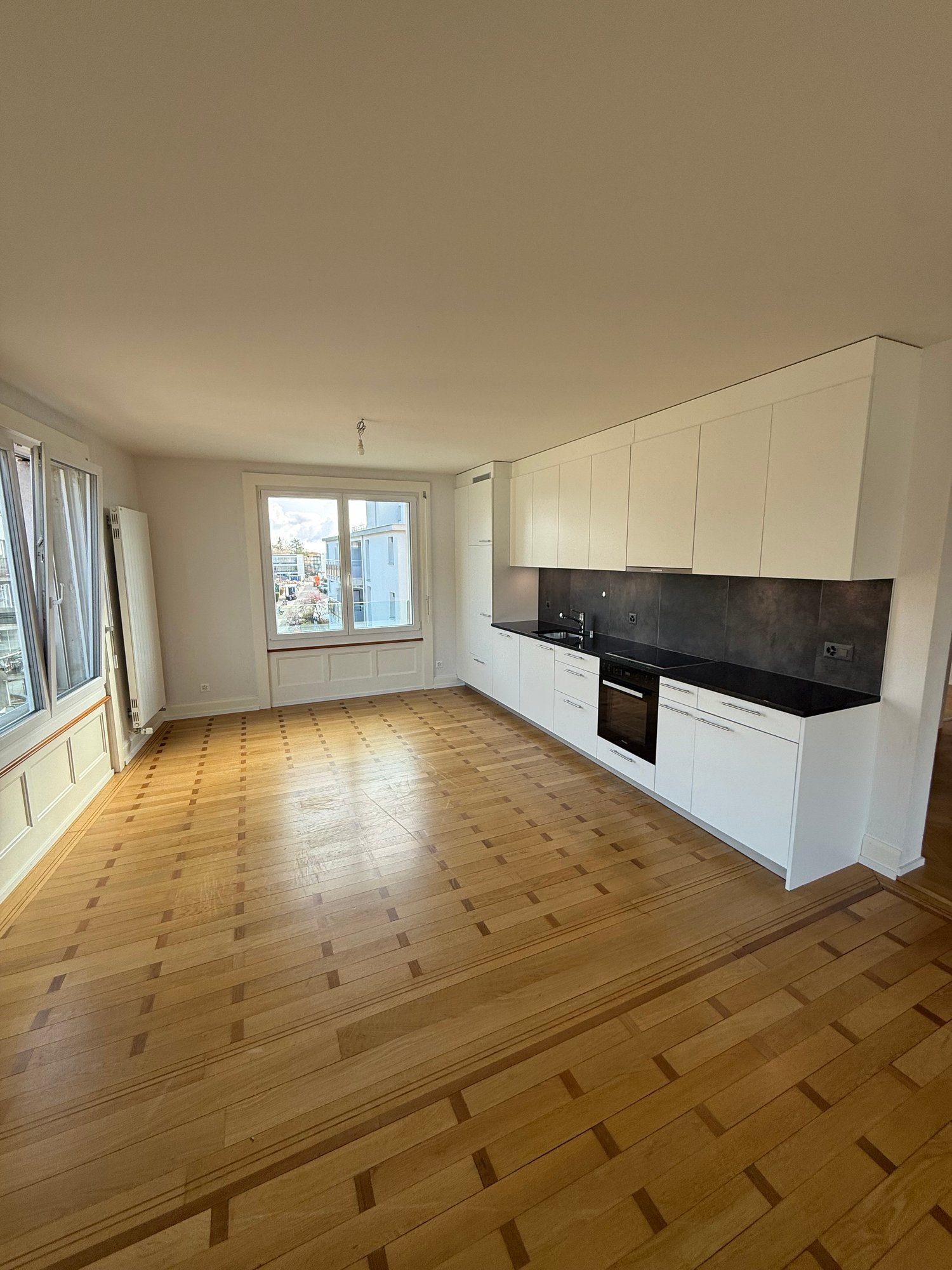Empty kitchen with wooden floor, white cabinets, black countertops, white appliances, large windows