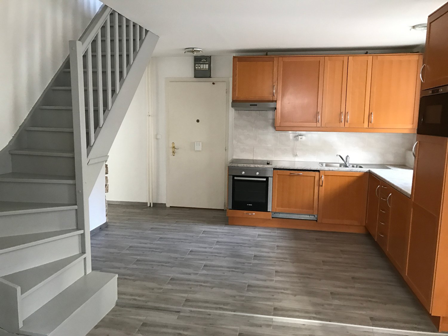 empty kitchen with wooden cabinets, tiled floor, white walls, staircase