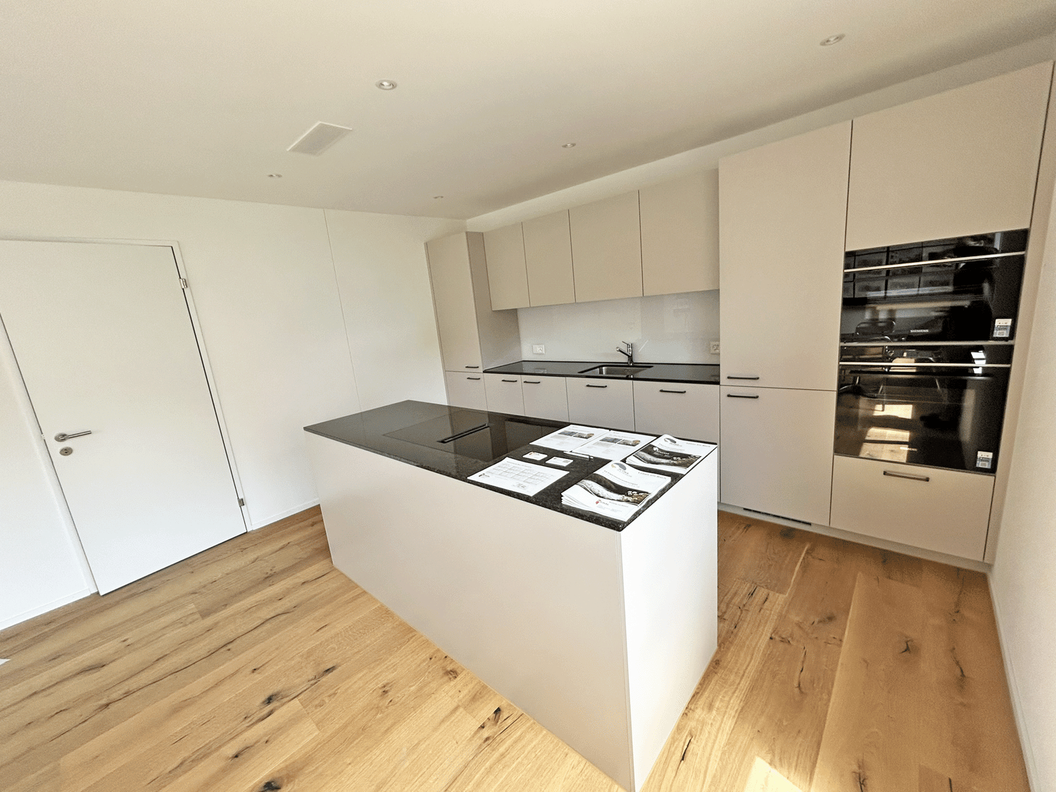 modern kitchen, white island, black granite countertop, white cabinets, central sink with faucet, embedded oven and microwave, hardwood floor