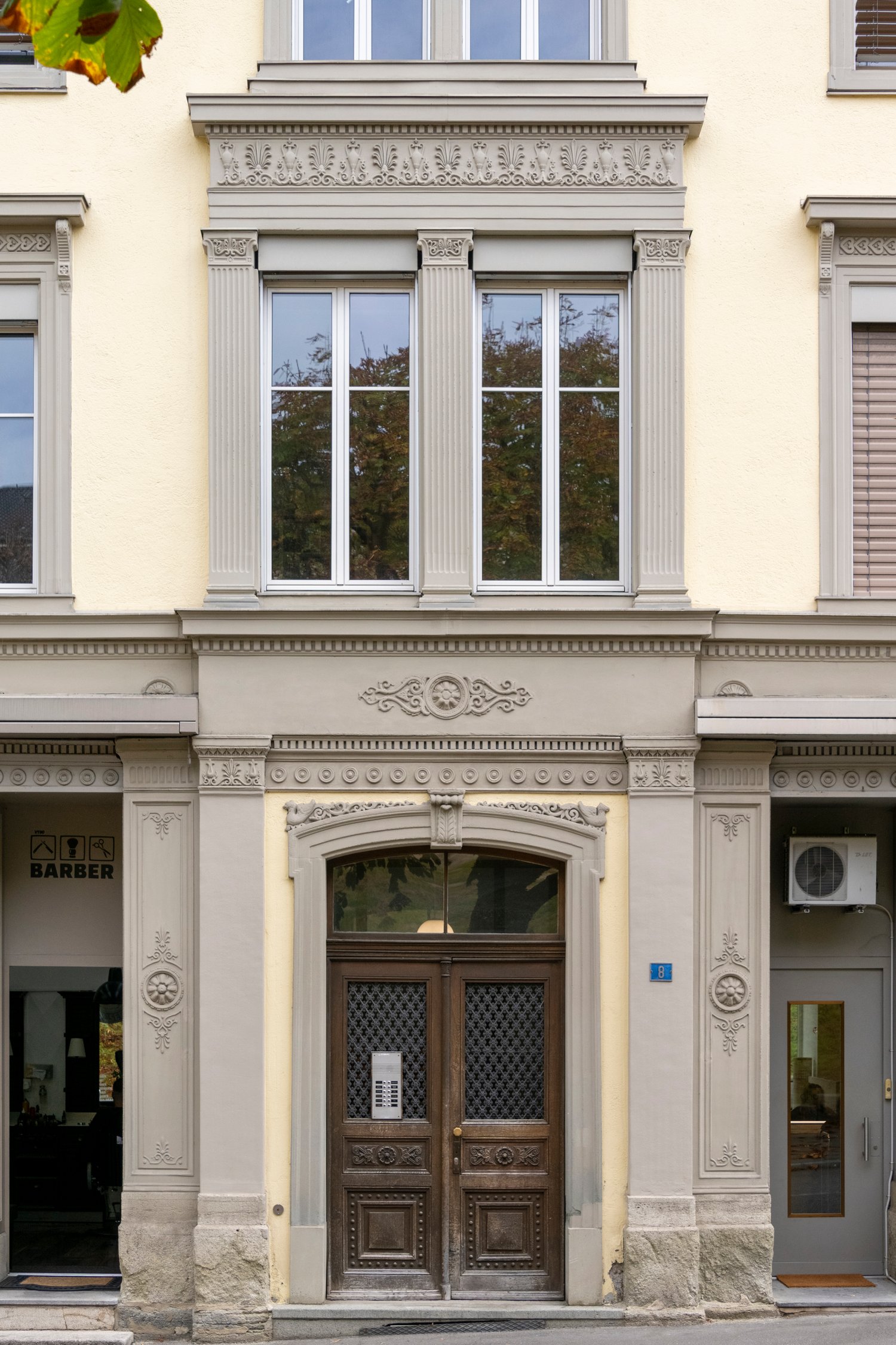 yellow facade, gray trims, two windows on each floor, wooden door with metal grille, a window on the first floor