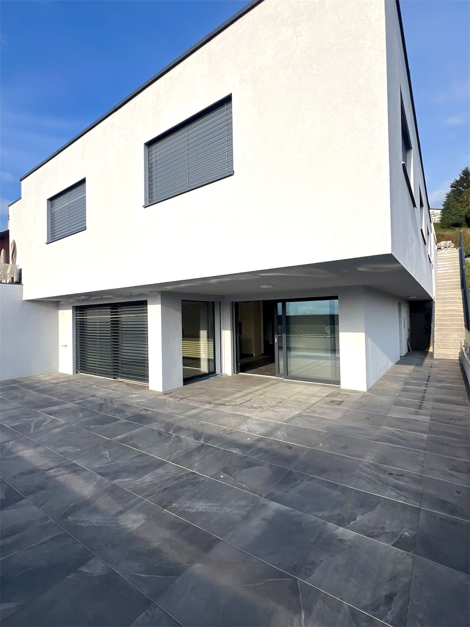 modern white house, glass doors, grey tiled terrace, garage with rolling shutter