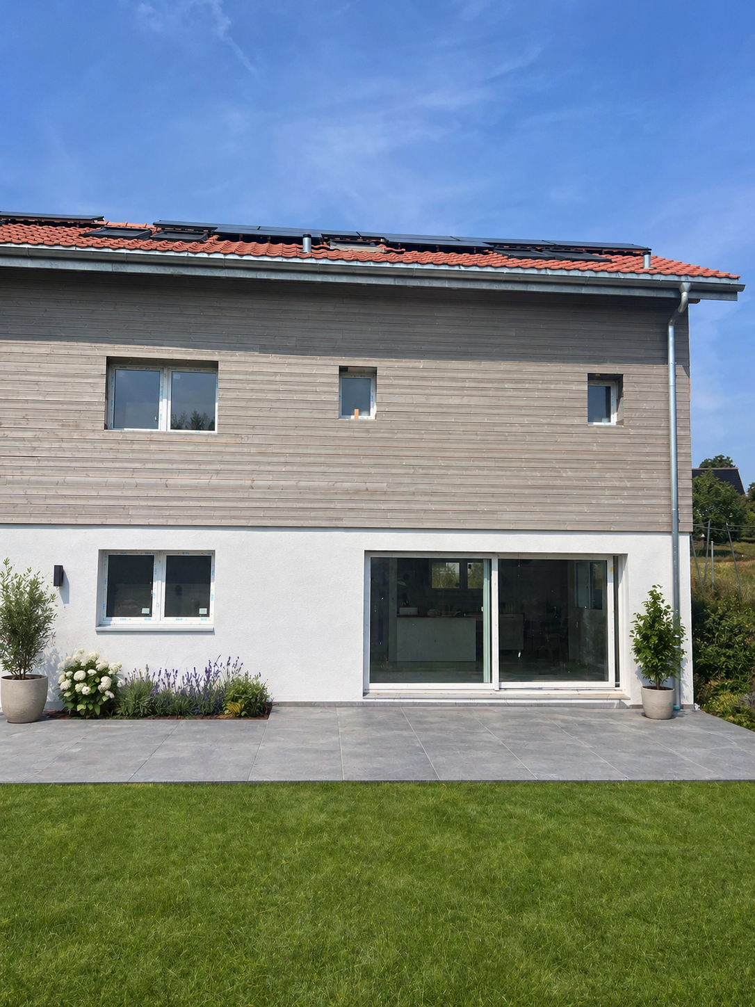 2 story house, wooden and white exterior, solar panels on roof, large glass doors, garden with plants