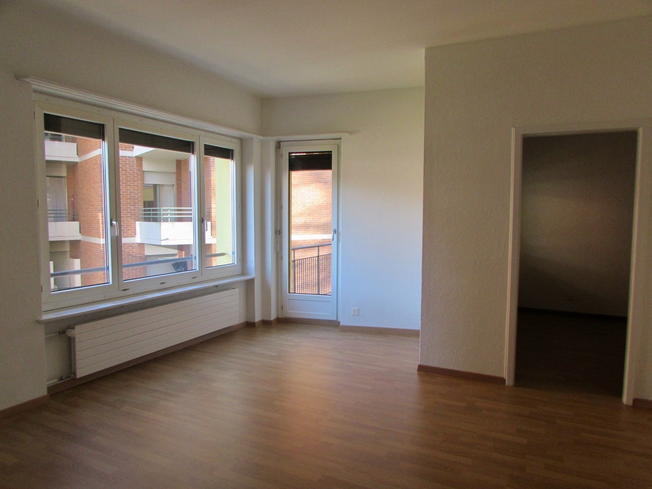 large windows, wooden floor, balcony, white walls, radiator, glass door