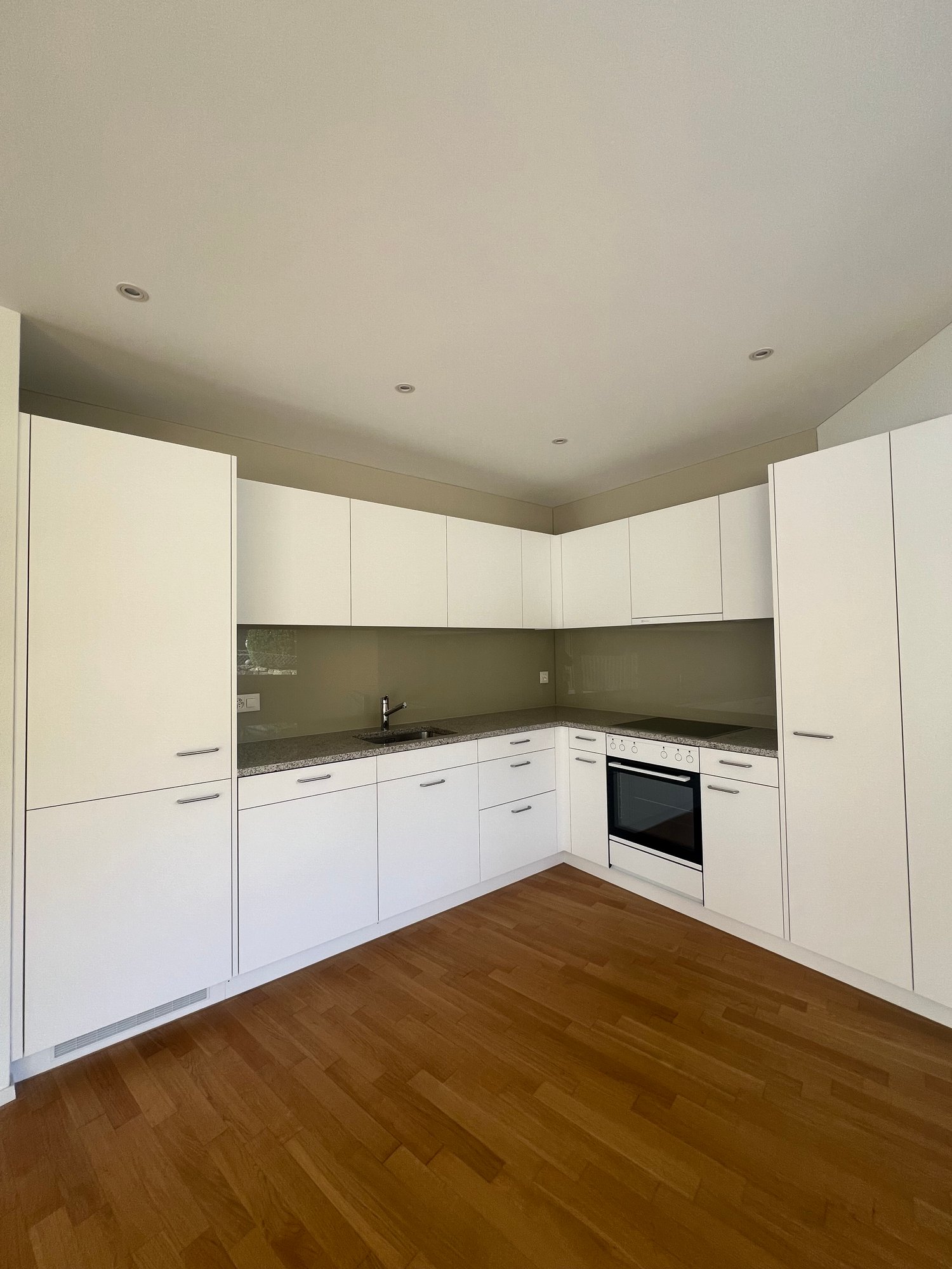 Modern kitchen with white cabinets, wooden floor, granite countertop, built-in dishwasher, built-in washing machine, stainless steel sink, oven, faucet