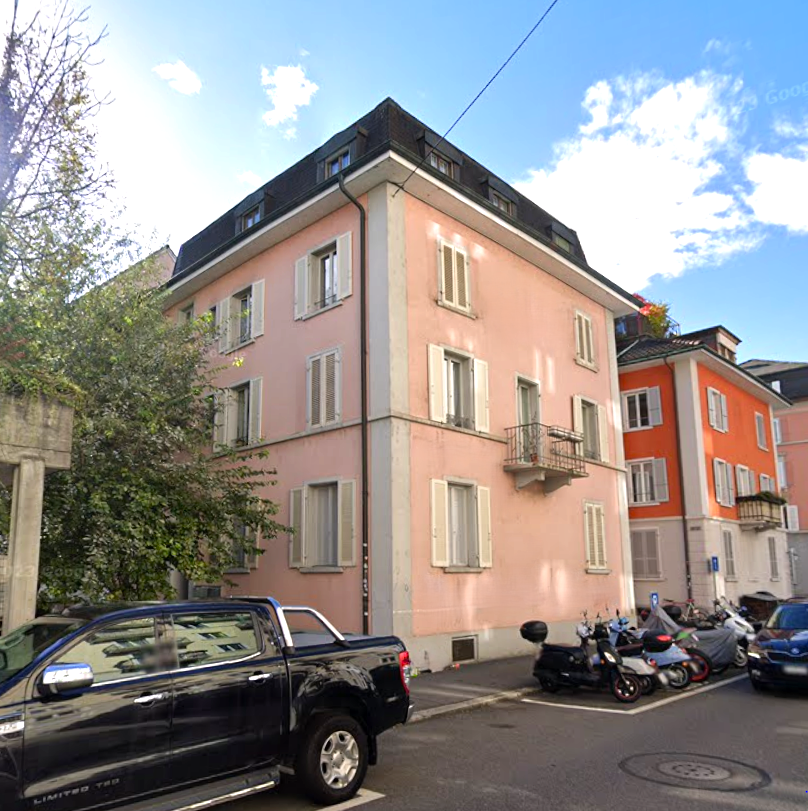 Multi-story building, pink exterior, white shutters, balcony, cars parked in front