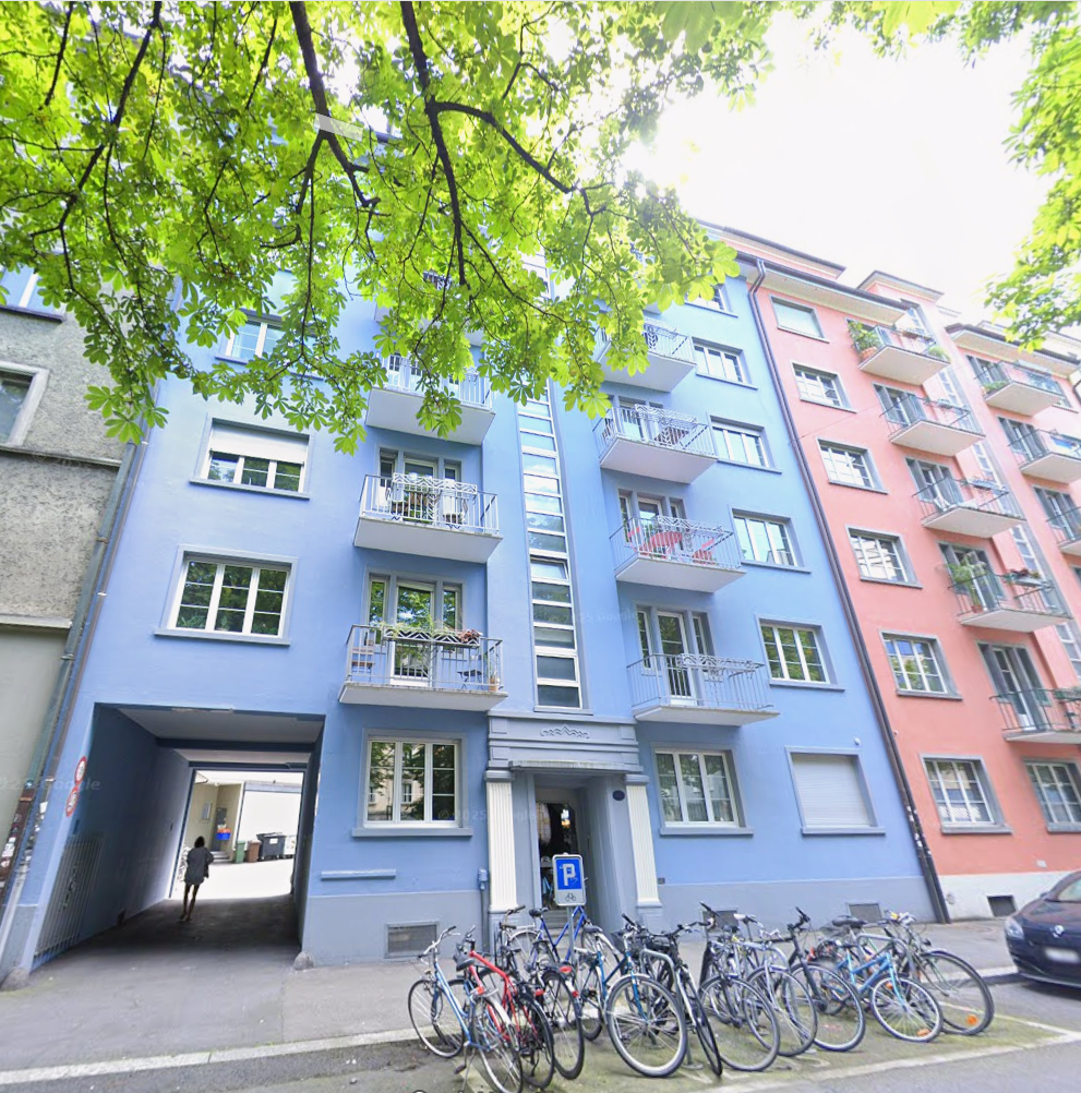 Blue building with 4 floors, balconies on each floor, bicycle parking in front of the building