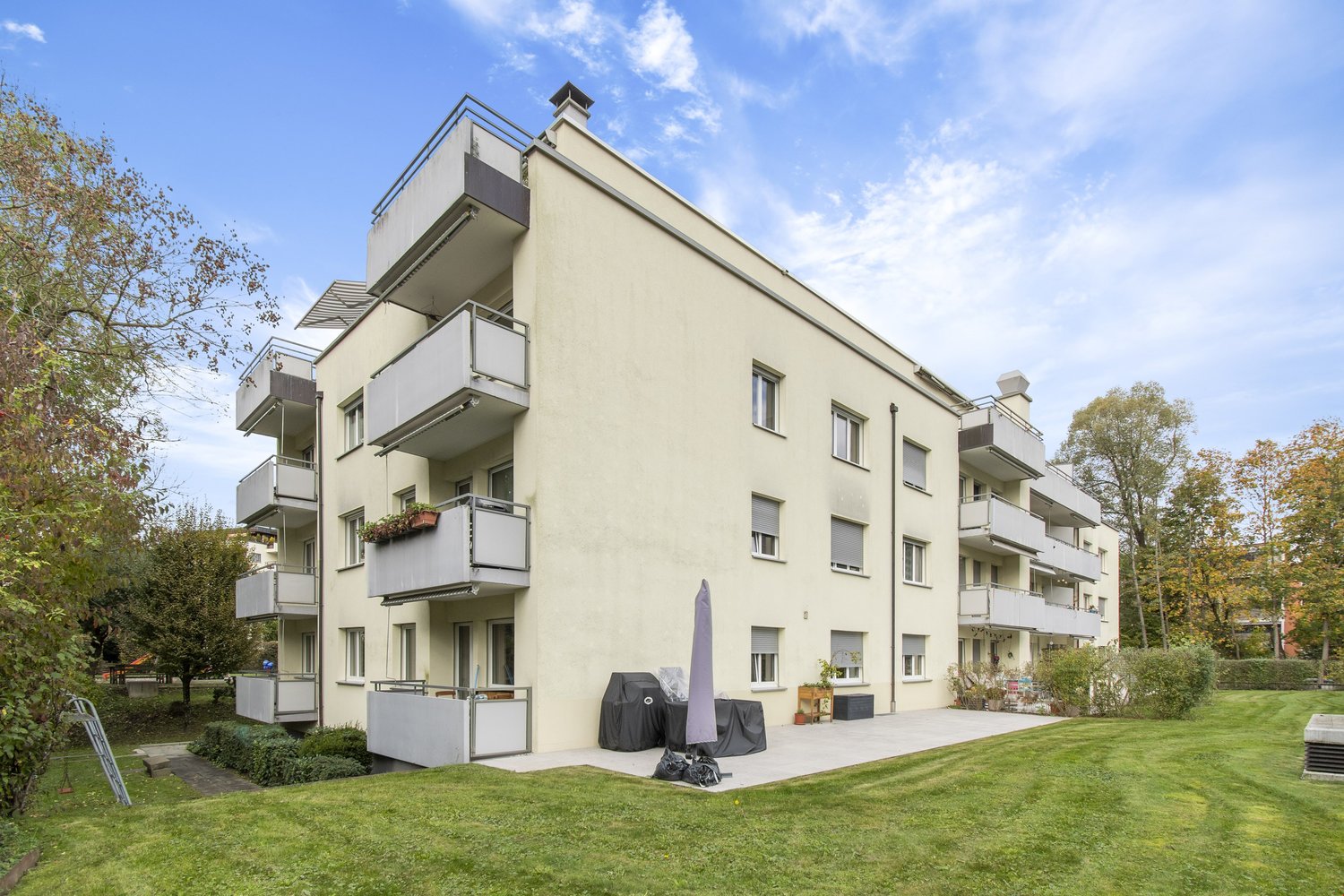 5-story apartment building, balconies on each floor, paved entrance area, plants, shrubs, lawn