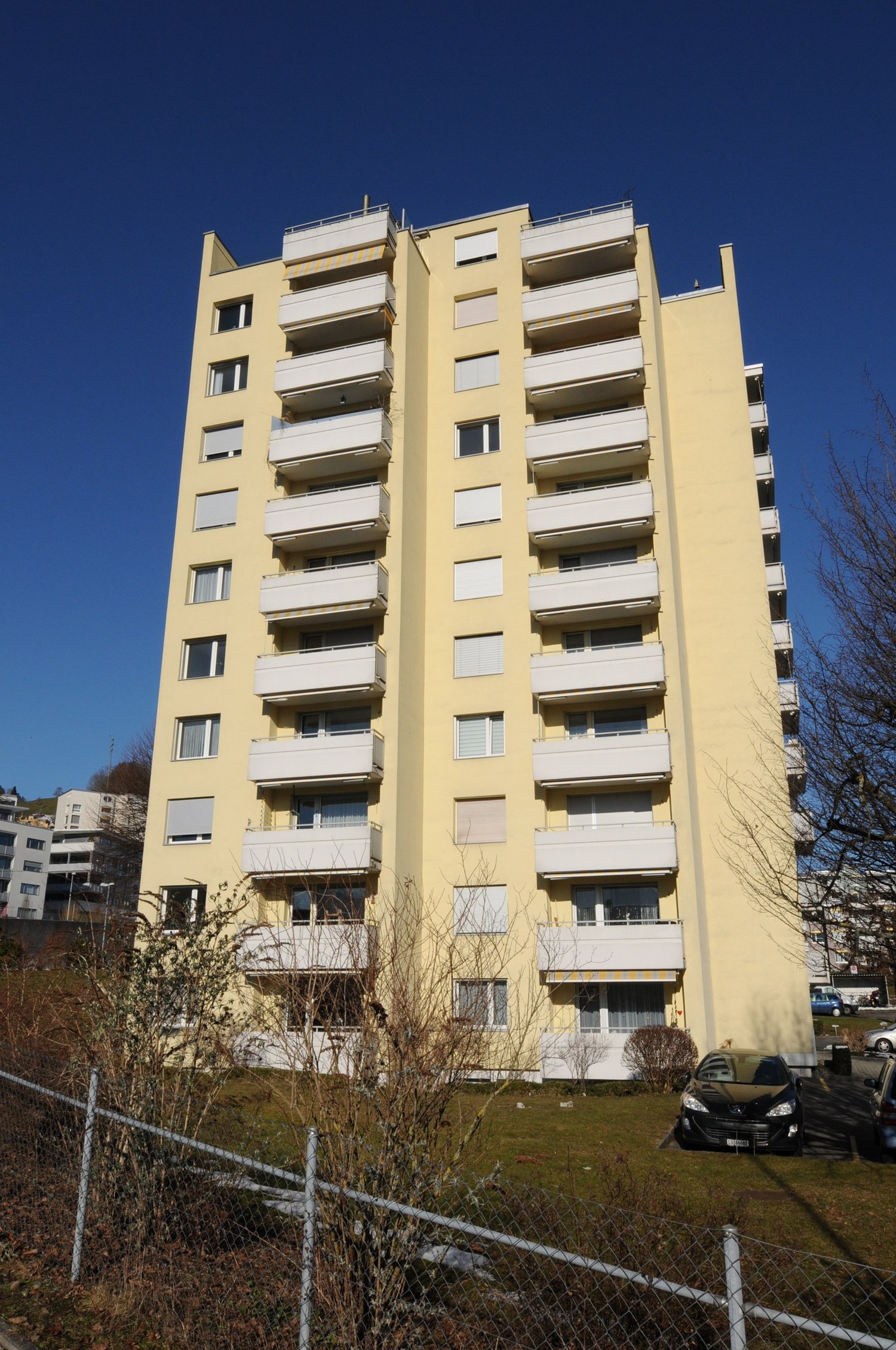 6 story yellow building, many windows, several balconies, parking area