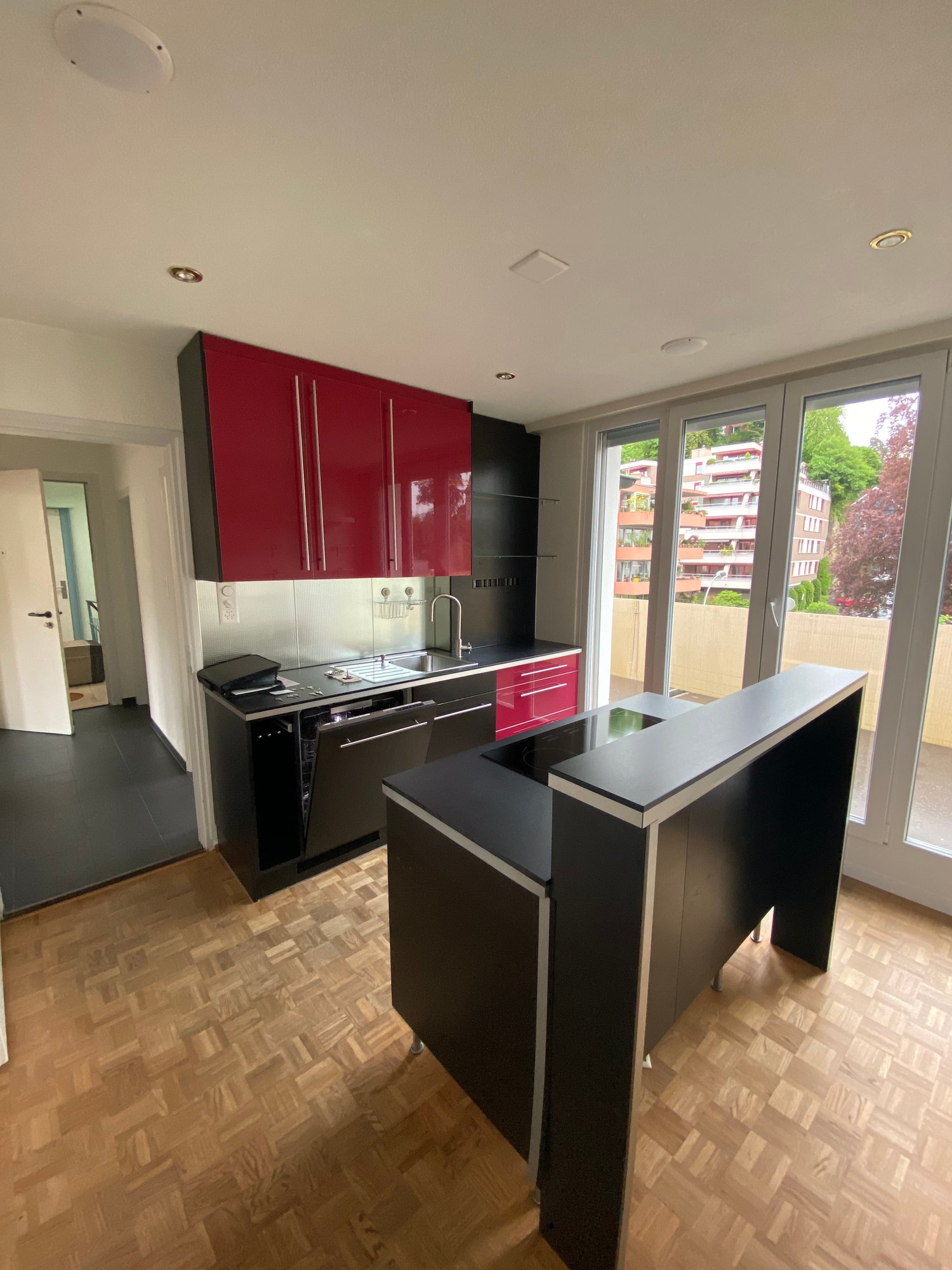 modern kitchen with red cabinets, black countertops, island, dishwasher, sink, faucet, wooden floor, sliding glass doors