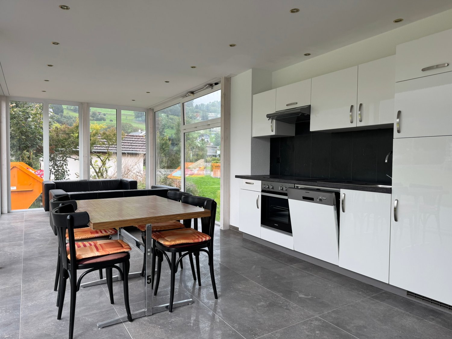 dining area with a wooden table and chairs, white cabinets, black countertops, oven, dishwasher, glass windows