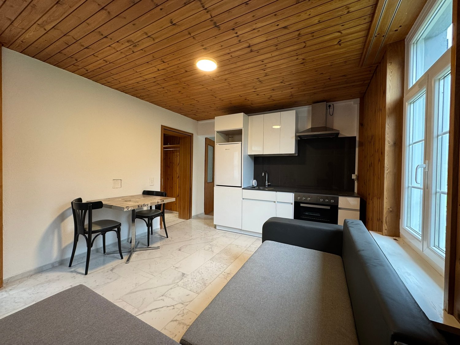 open-plan living room and kitchen, large window, wooden ceiling, dining table, sofa, marble flooring, refrigerator, oven