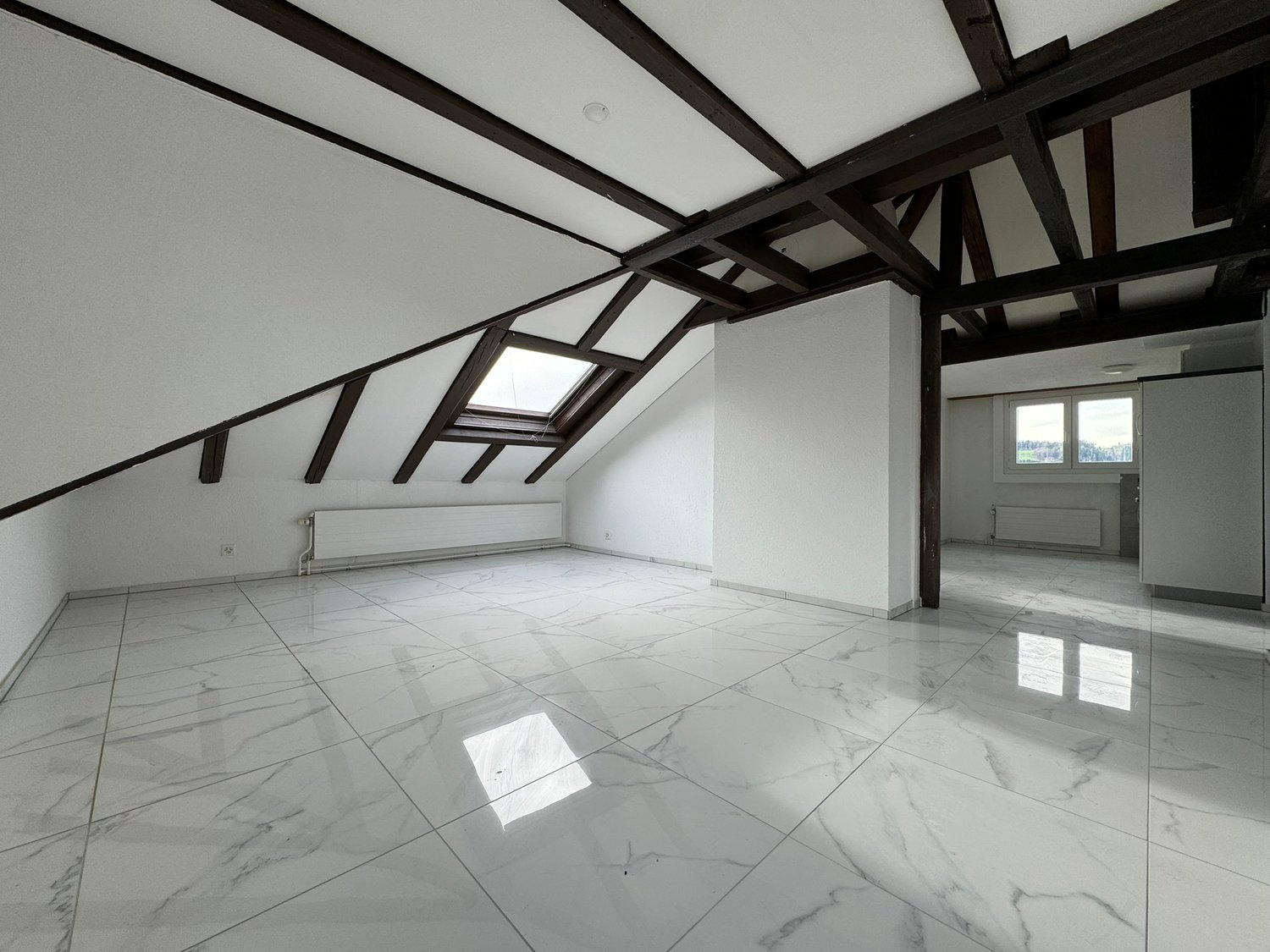 an attic room with a white tiled floor, dark wooden beams on the ceiling, skylights, a white pillar and a heater