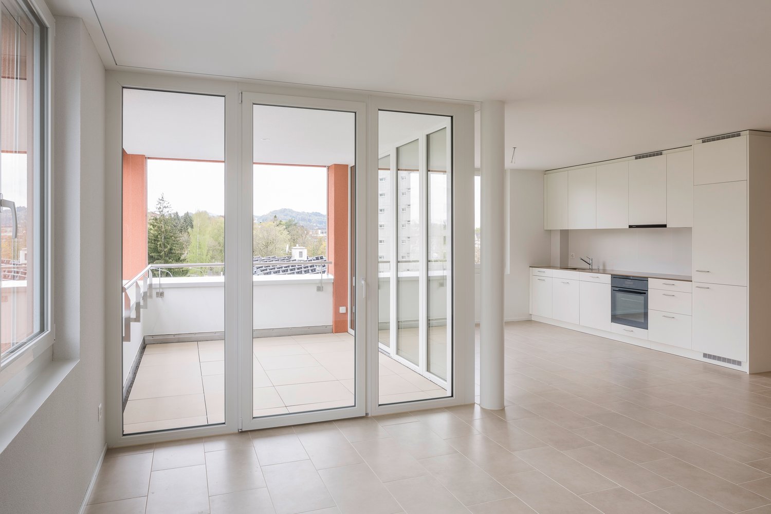 Large sliding glass doors leading to a balcony, modern kitchen, beige tiles throughout