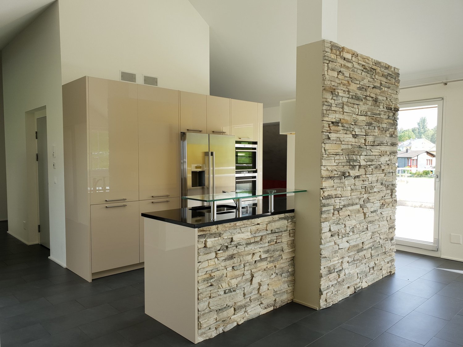 modern kitchen with large island, stone wall, glass countertops, built-in appliances