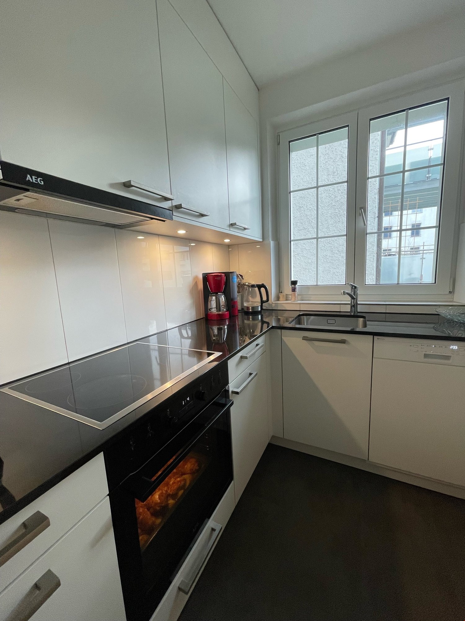 modern kitchen, white cabinetry, black countertops, induction stove, oven, dishwasher, sink, coffee maker, kettle, windows