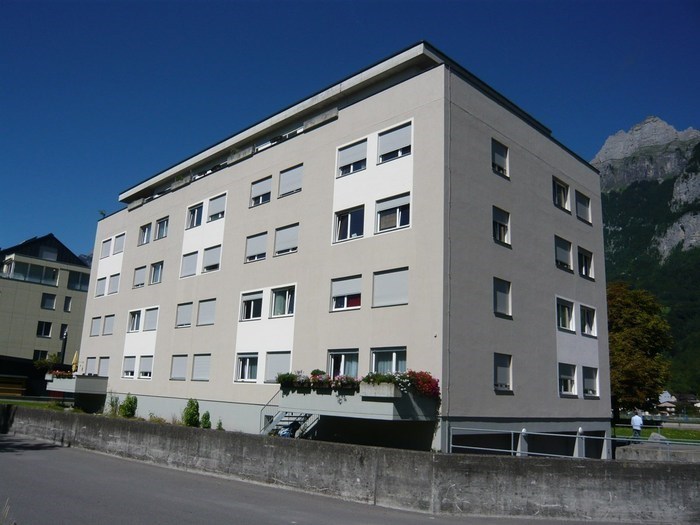 5 story residential building, concrete walls, windows with shutters, balcony with plants