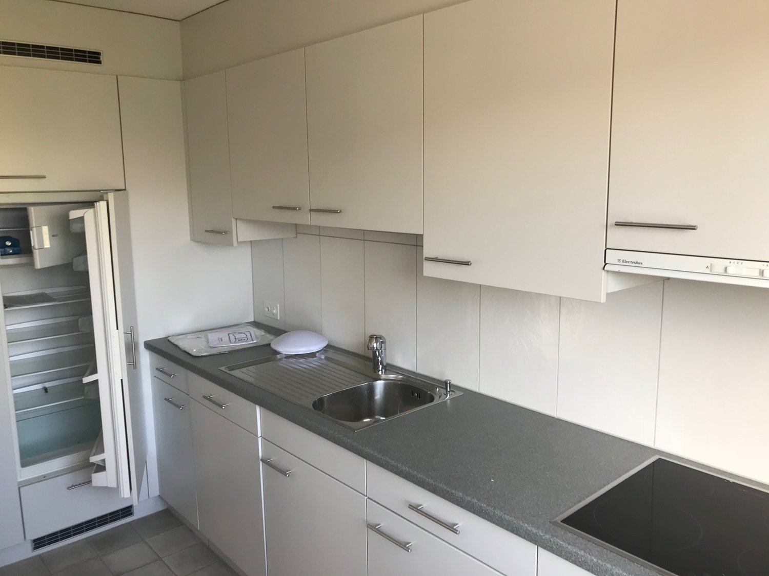 Modern kitchen with white cabinets, gray countertops, stainless steel sink, and a built-in dishwasher