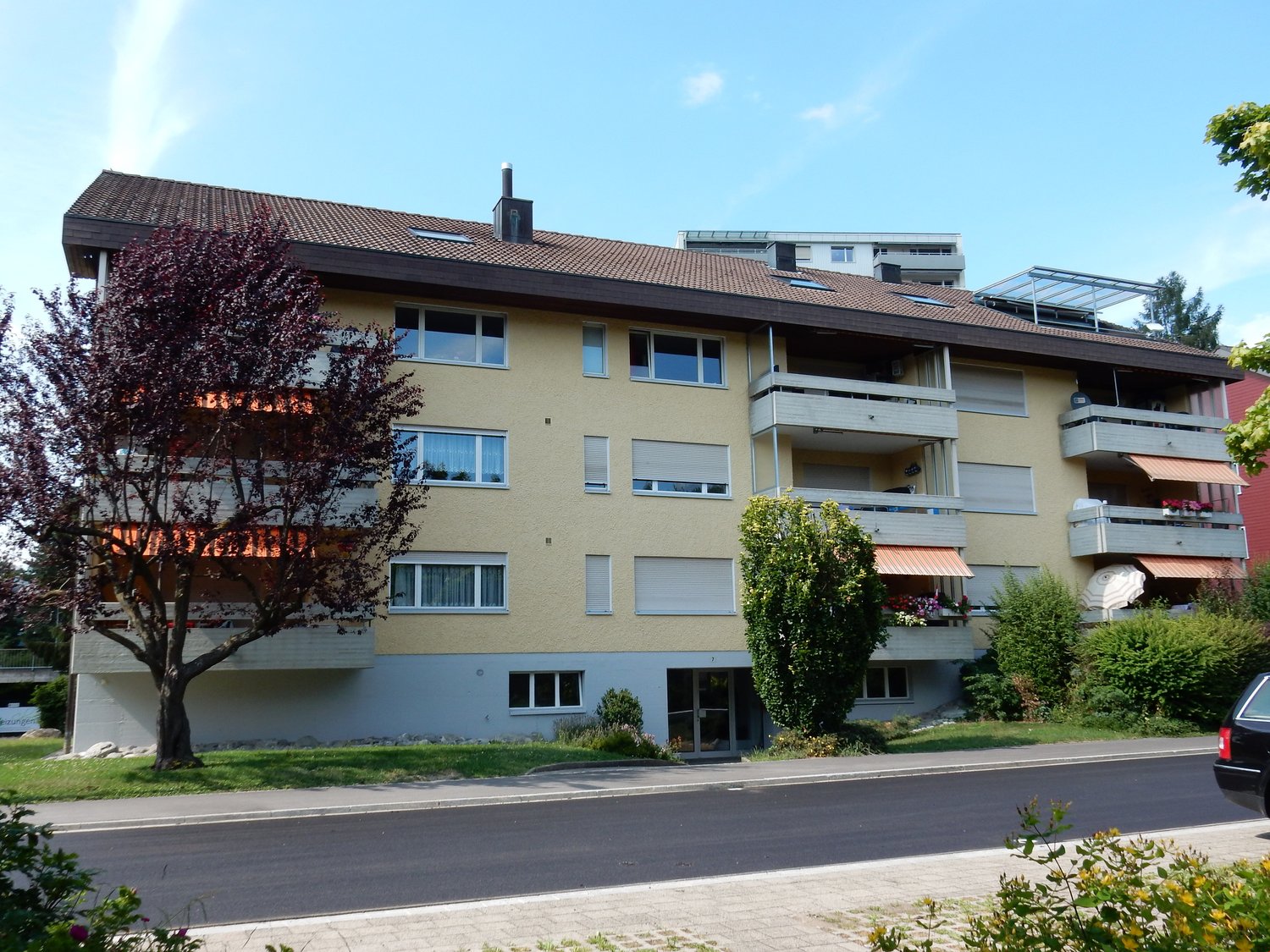 4-storey apartment building, yellow painted exterior, multiple balconies, green tree in front, paved driveway