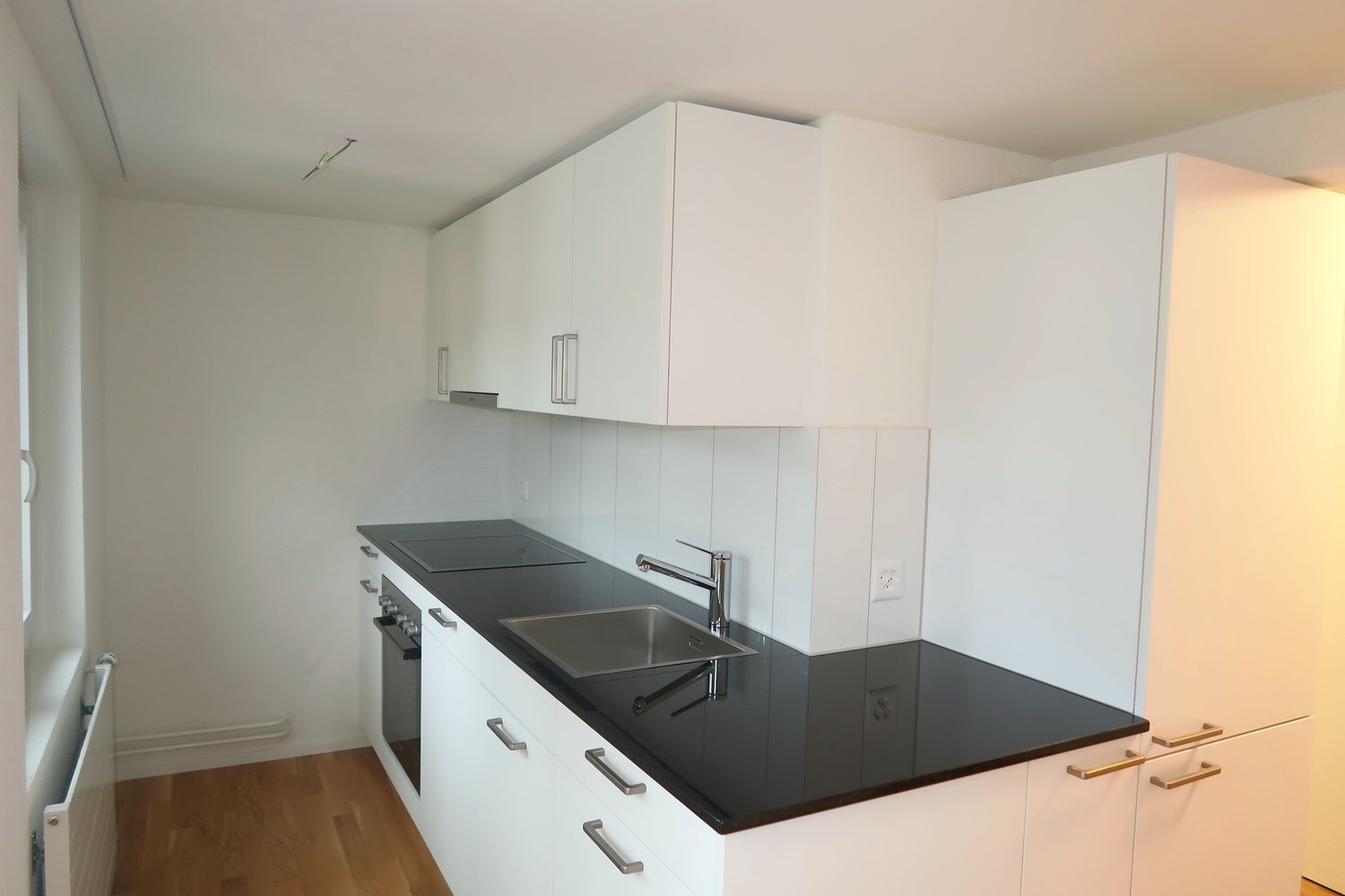 kitchen with modern white cabinets, a black granite countertop, stainless steel sink, and a faucet.