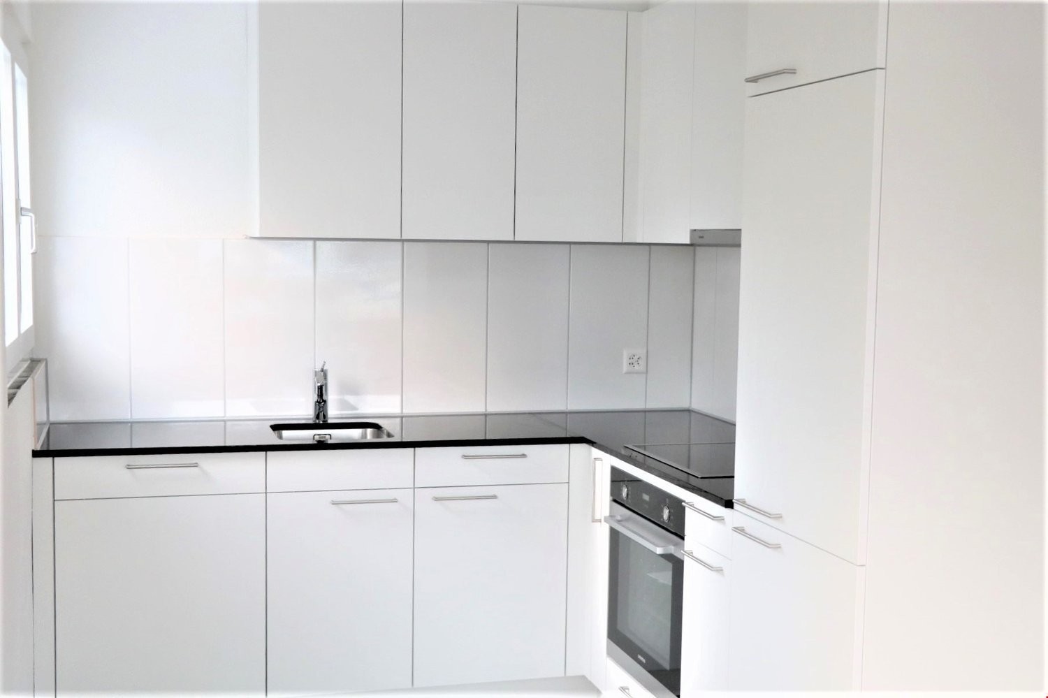 Fully equipped kitchen with white cabinetry, black countertops, integrated oven and dishwasher, stainless steel sink, and a window