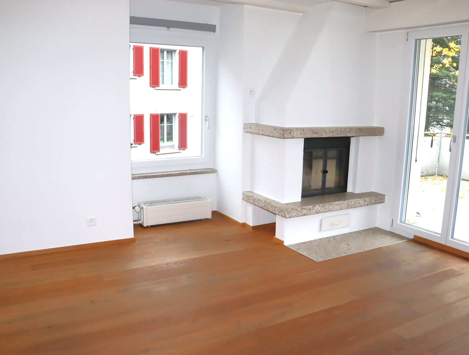 Fireplace, wooden floor, white walls, windows with red shutters, sliding glass doors, radiator