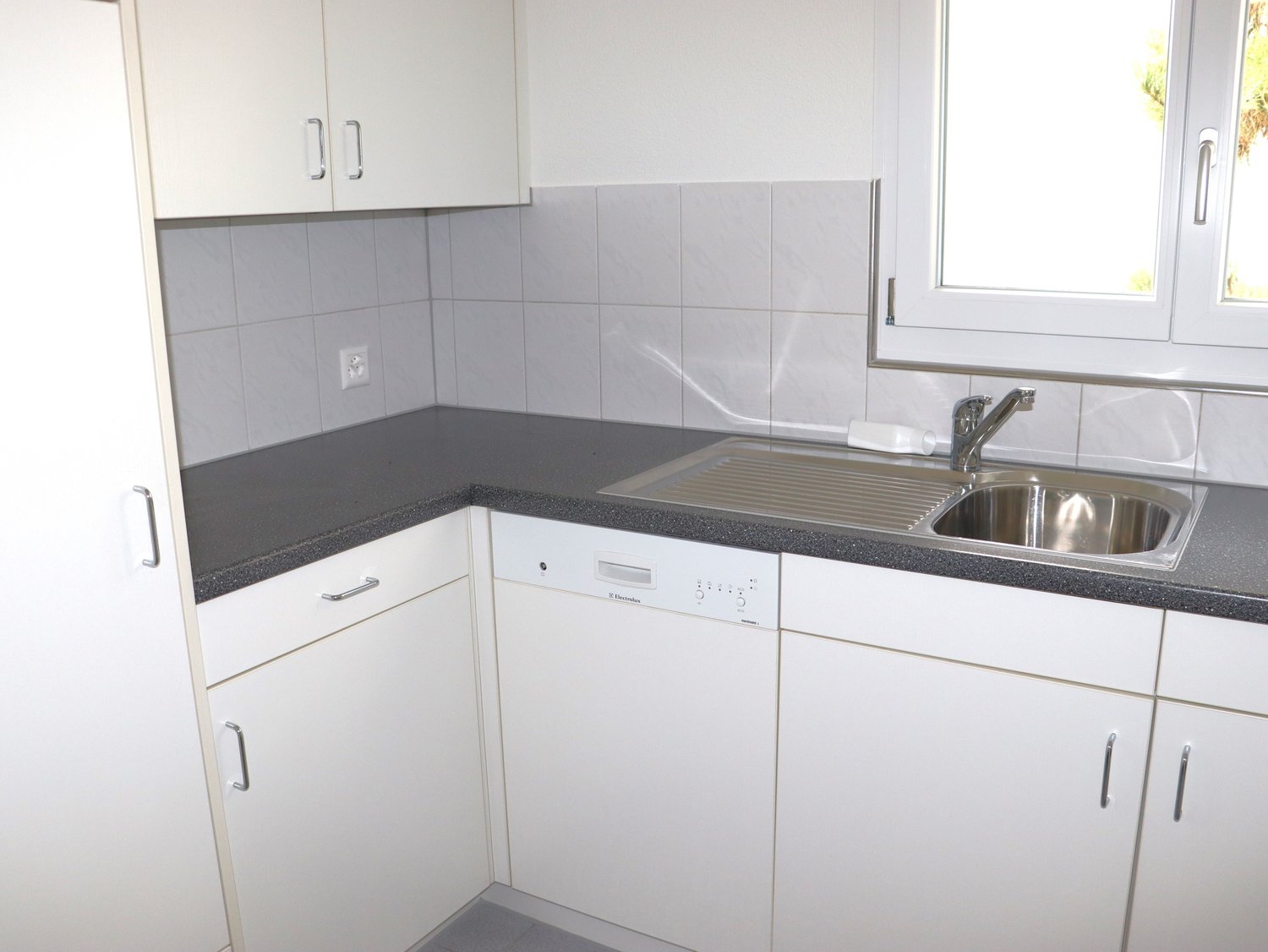 a clean kitchen with white walls, cabinets, countertops, a sink, dishwasher, and a washing machine