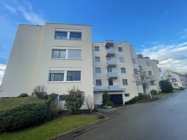 3-story apartment building with white exterior, multiple balconies, and a parking area in front