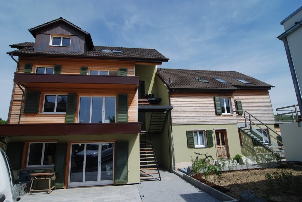 A two-story wooden house with green shutters and glass walls