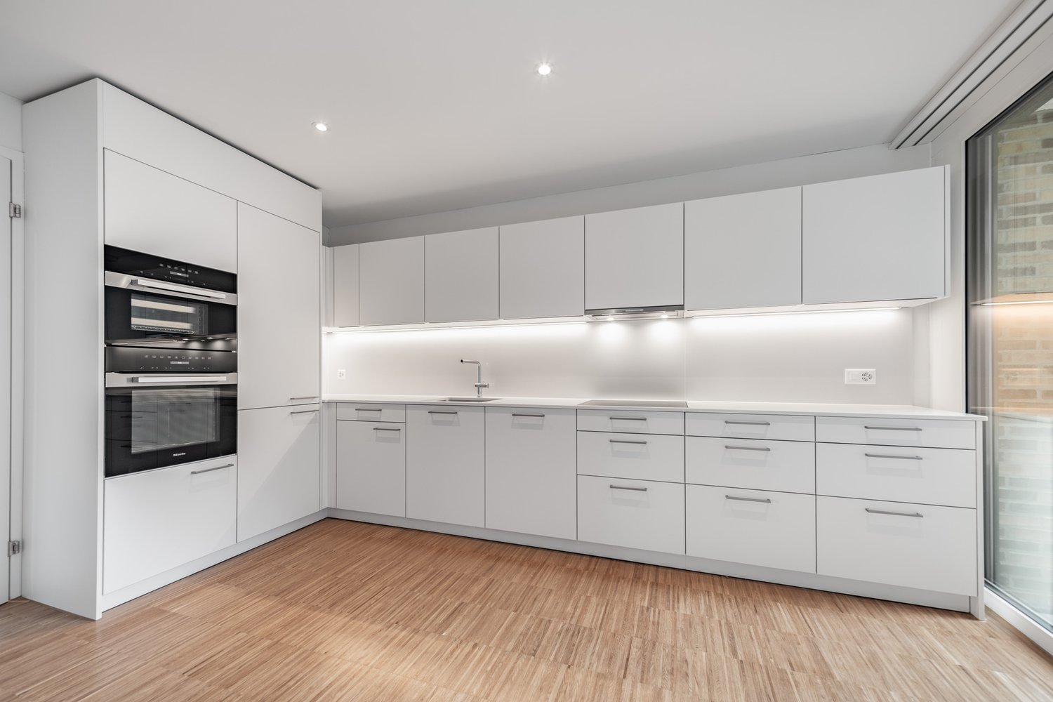 Spacious modern kitchen with white cabinets, built-in appliances including a dishwasher, and hardwood flooring