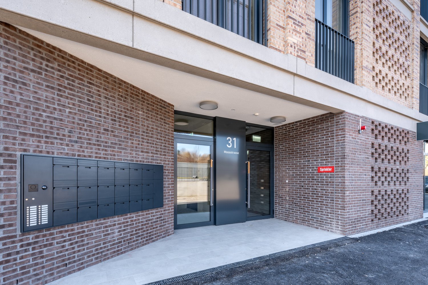 Exterior entrance with mailboxes, glass doors, brick wall, concrete floor
