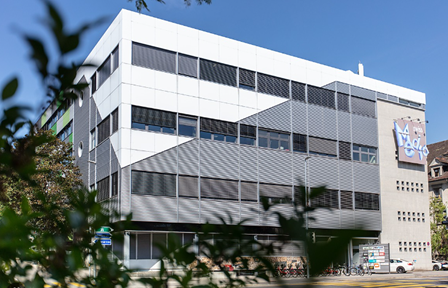 A multi-story office or commercial building with a modern, minimalist design. The building has a white exterior with large windows and a prominent entrance.
