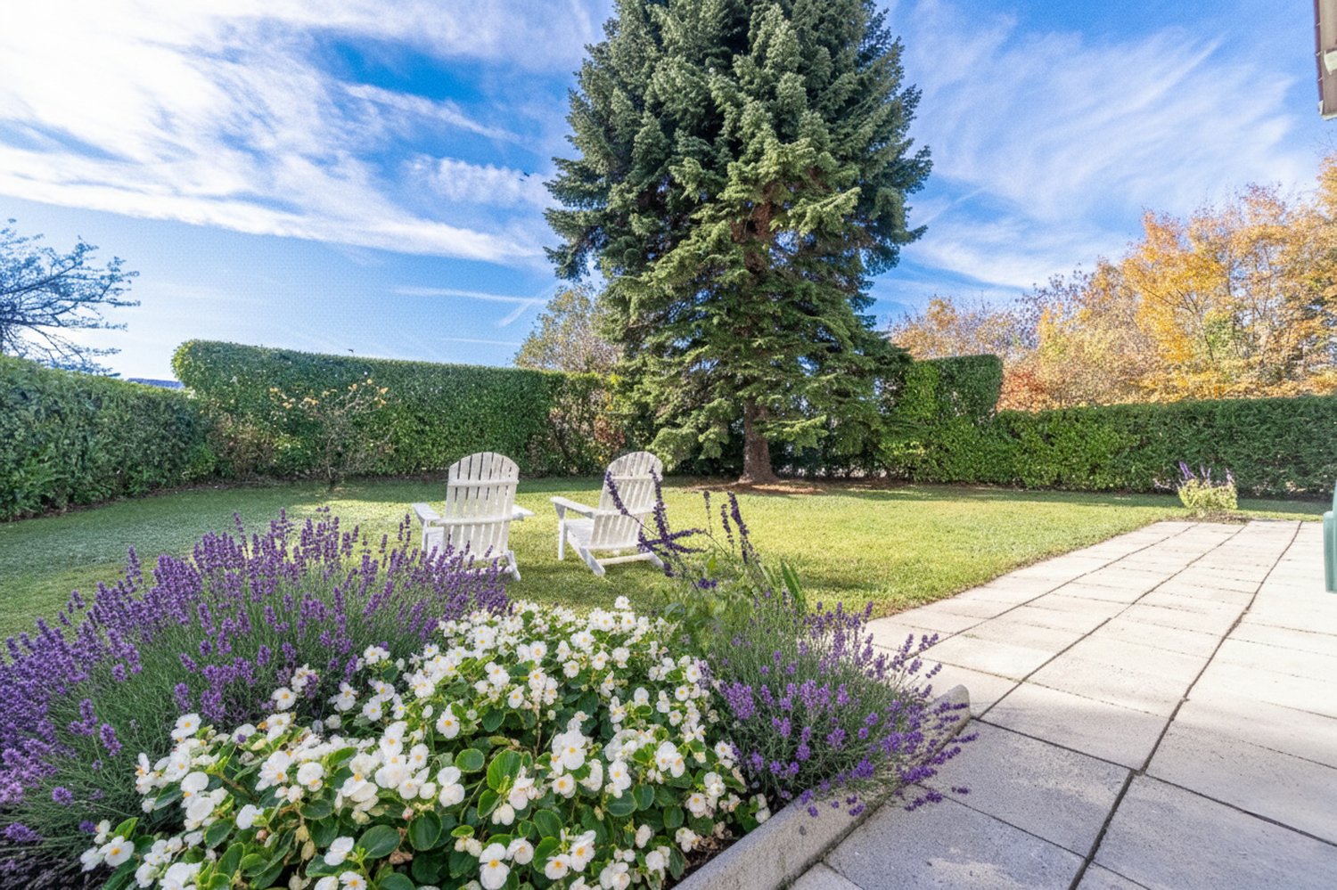 well-maintained garden with lawn, shrubs, and two white chairs