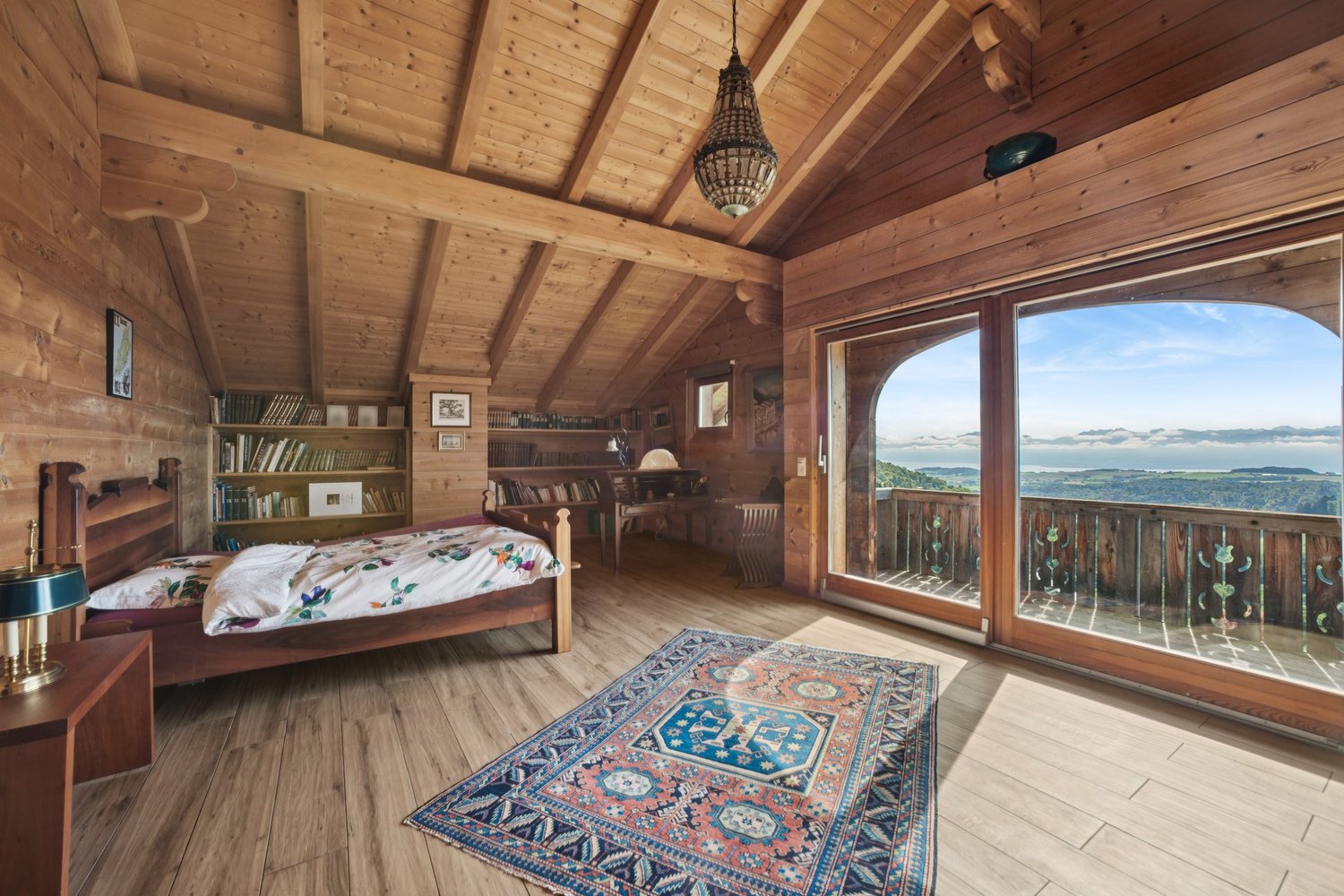 bedroom with wooden bed, rug, wooden wall and flooring, large window with wooden balcony, lamps, desk, bookshelves