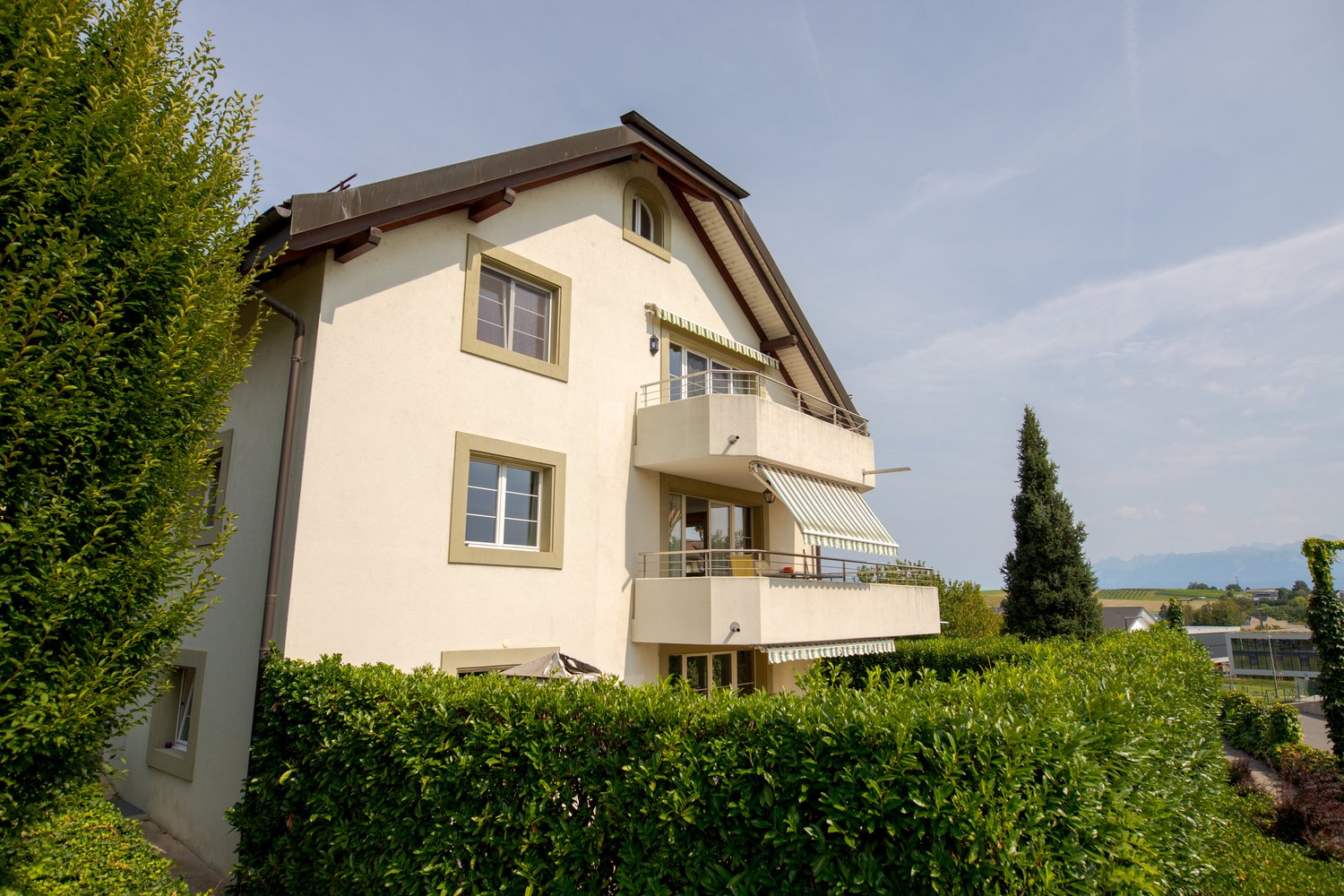 2 story house, cream exterior, brown roof, white framed windows, covered balcony with awning