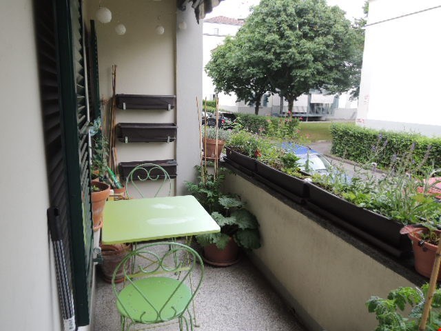 green table, green chairs, floor, balcony, various potted plants, street, parked car