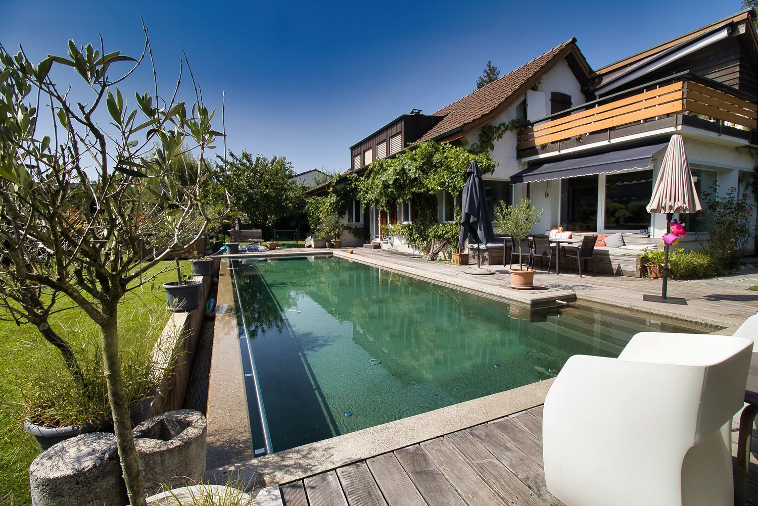 detached house, 3 story, brown roof, large pool in garden, white chairs on deck