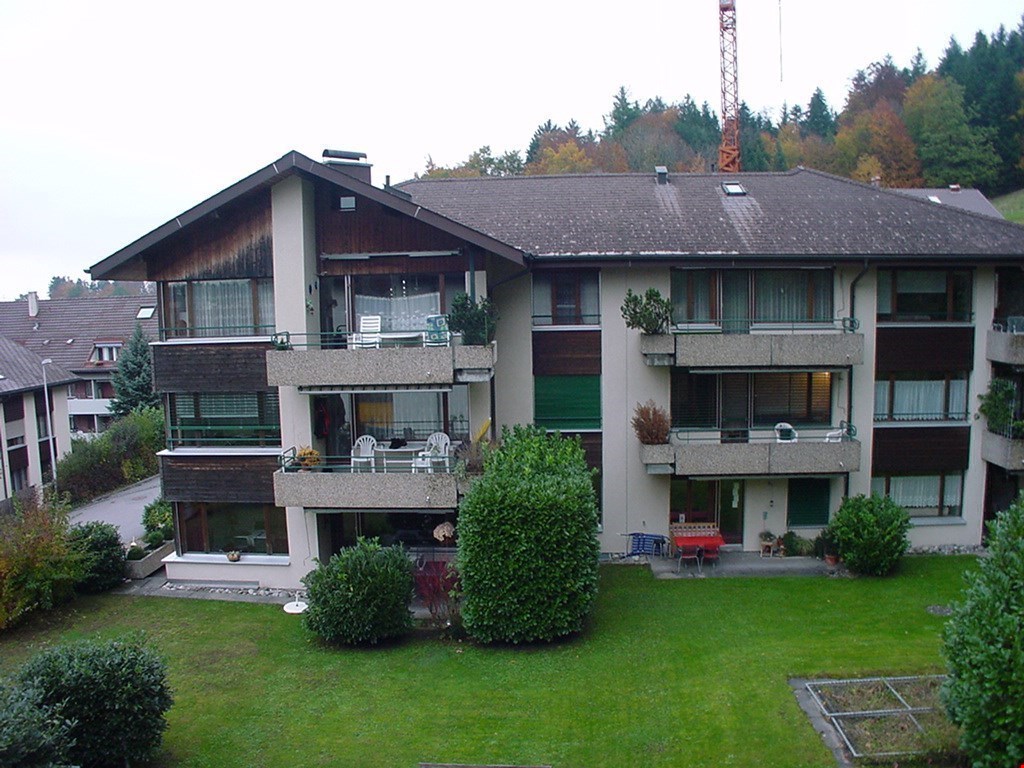 Three story building with several balconies, red furniture, garden