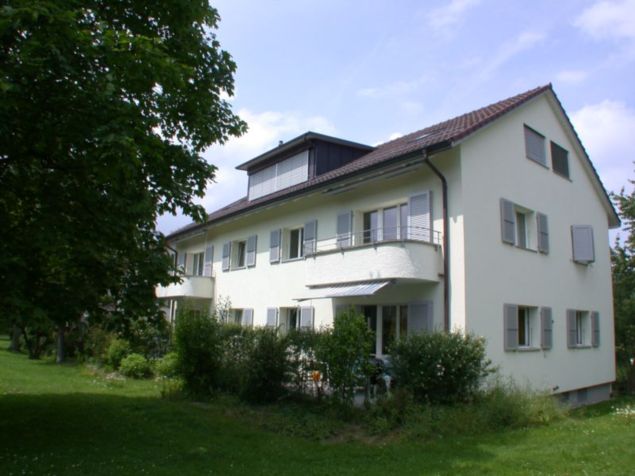 Two story house, white exterior, brown roof, many windows, balcony, garden