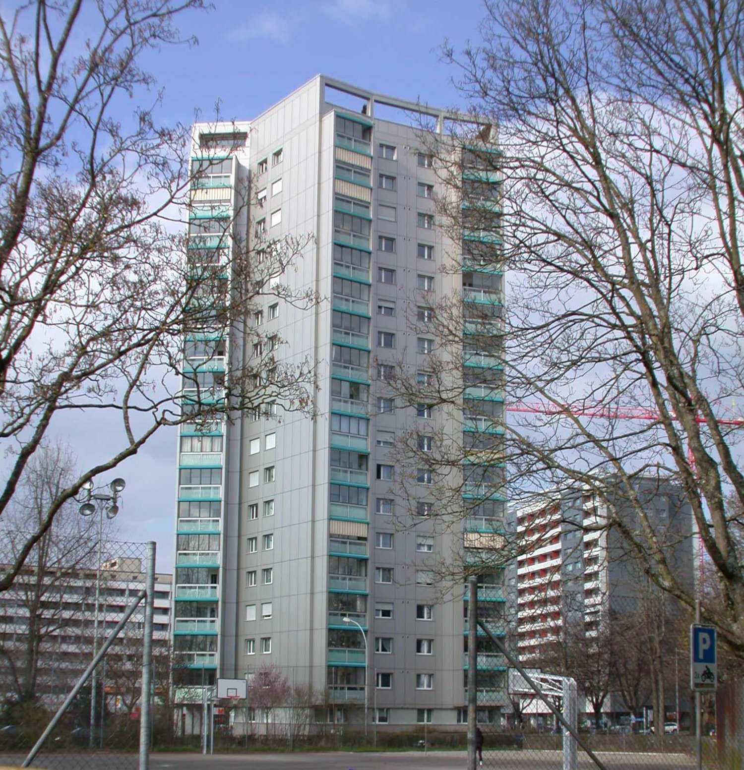 multi-storey residential building, balconies on each floor, grey exterior, multiple windows, parking in front