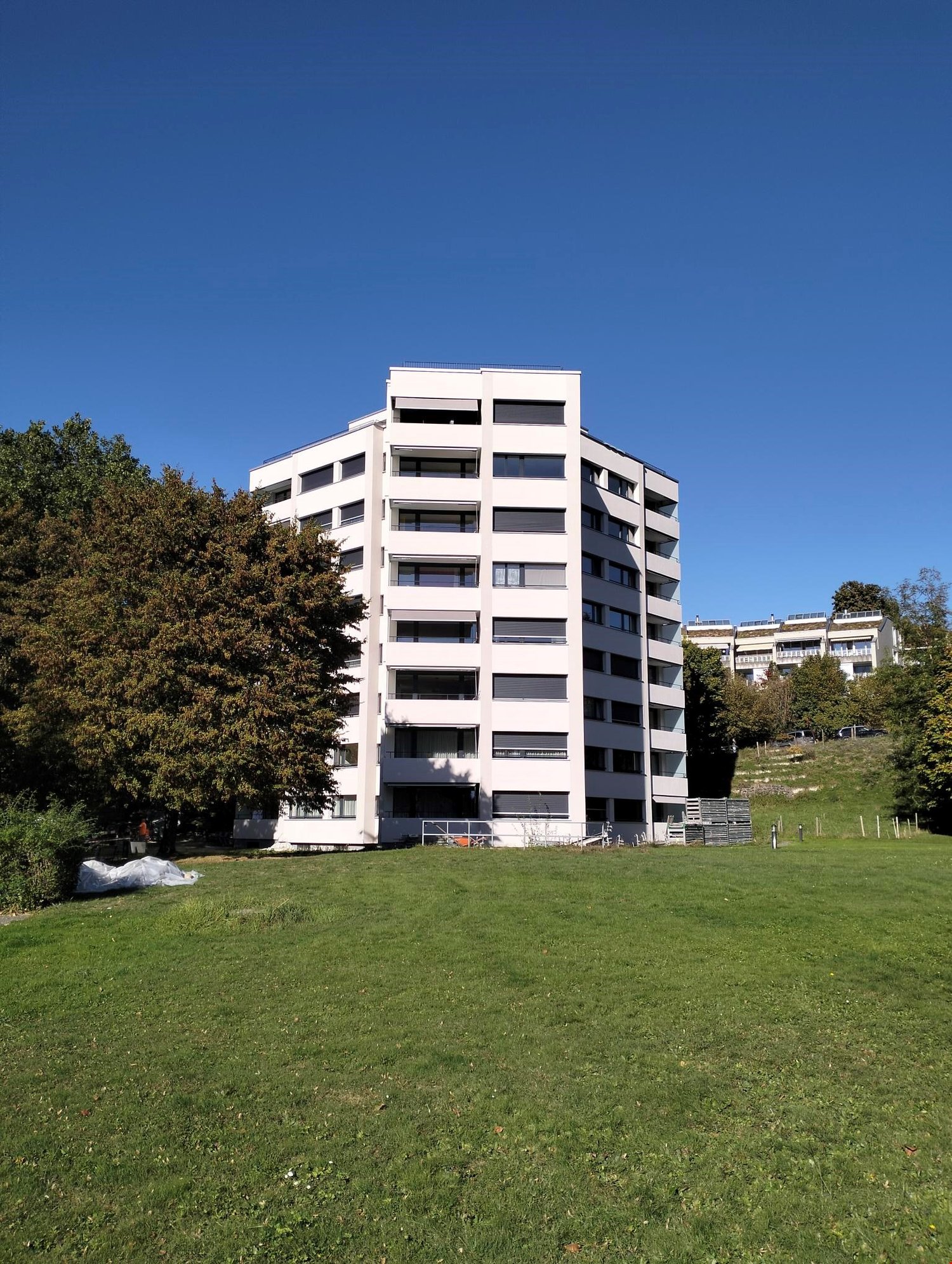 Modern building with multiple windows, balcony, white painted, well maintained grass lawn, trees