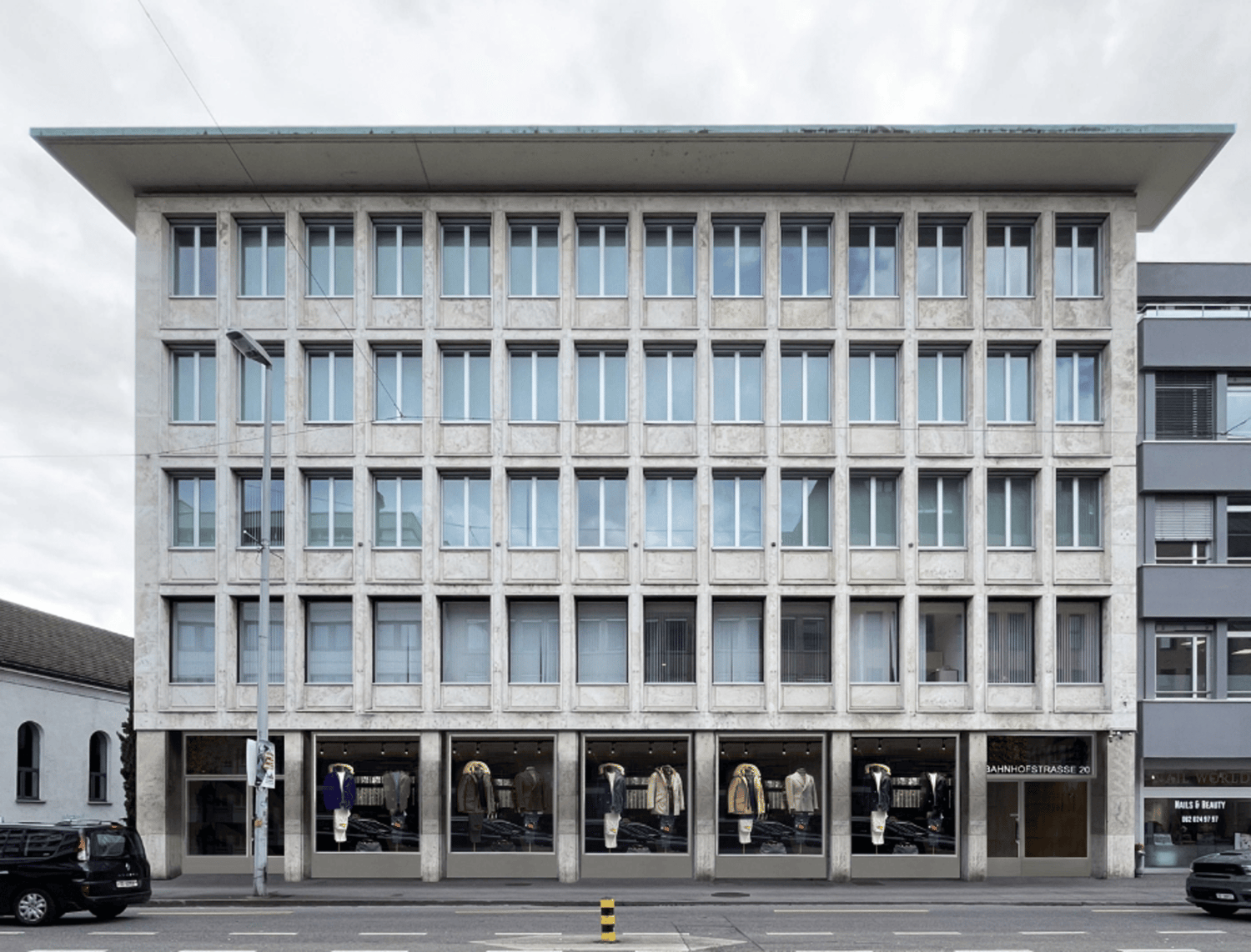 Concrete building, large windows, multiple floors, modern architecture, commercial facade, shopfronts, street-level entrance, grey exterior