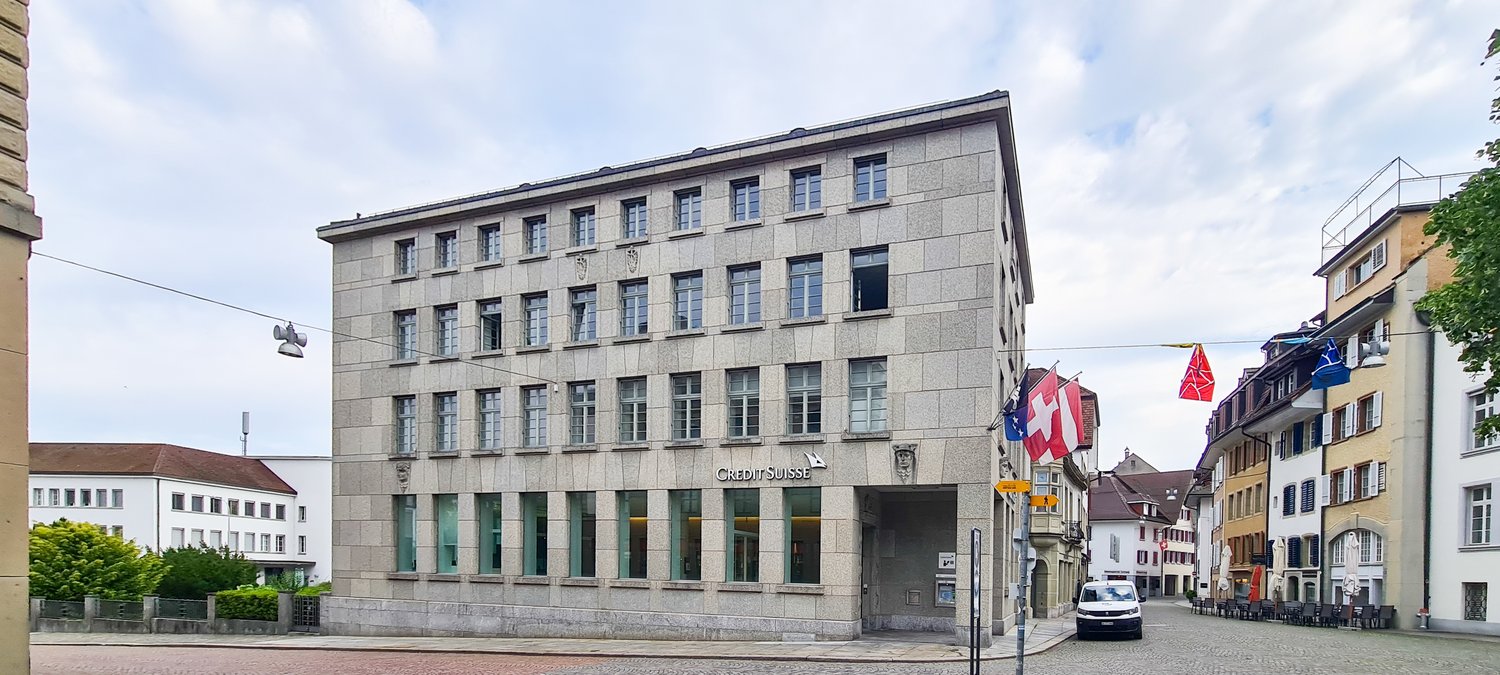 3 story building, concrete exterior, many windows, entrance at street level, flag at entrance