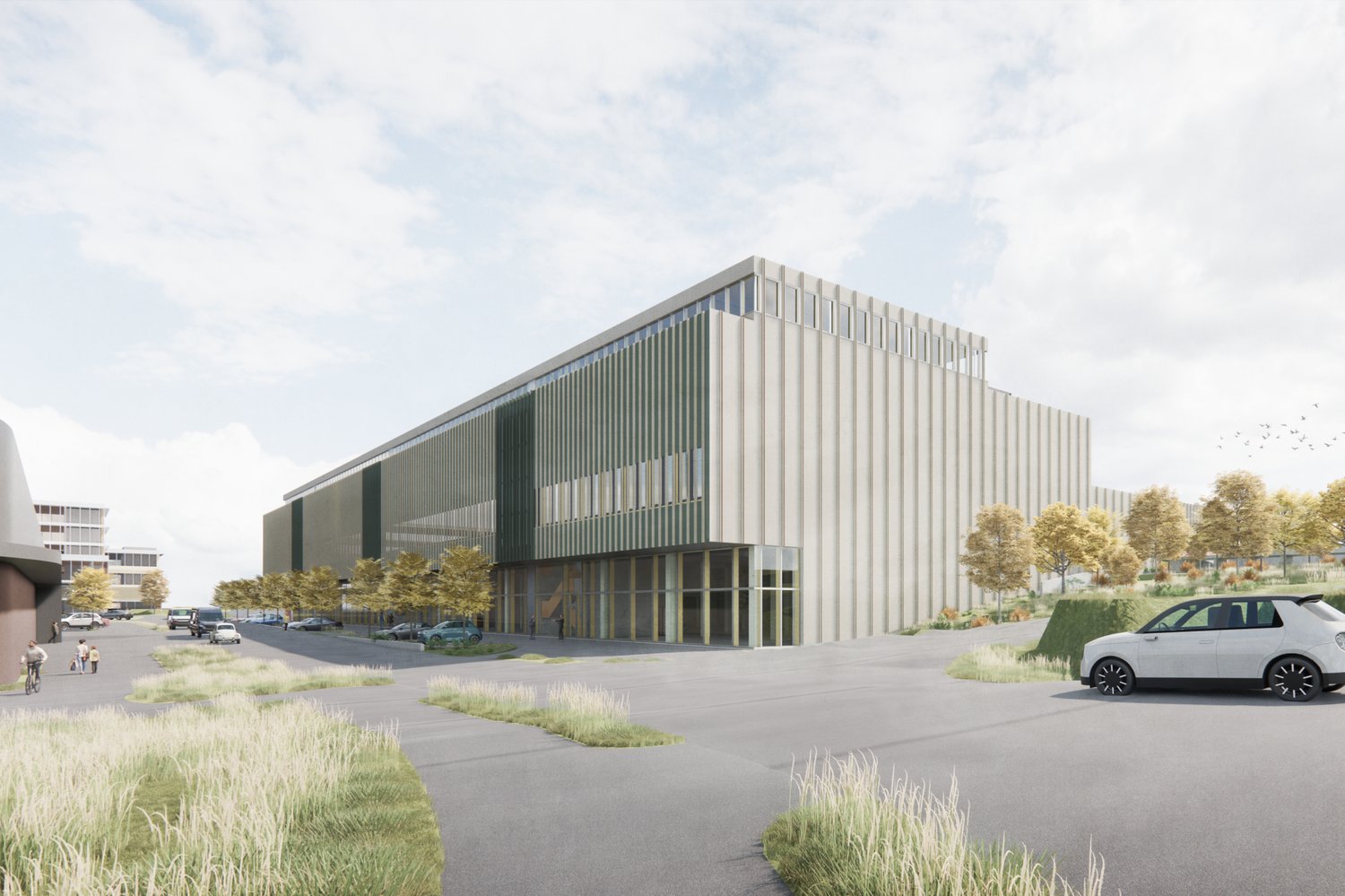A large modern industrial or commercial building with a rectangular, multi-story design featuring a mix of concrete and glass materials. The building has a sleek, contemporary architectural style with vertical lines and a prominent entrance. The surroundi