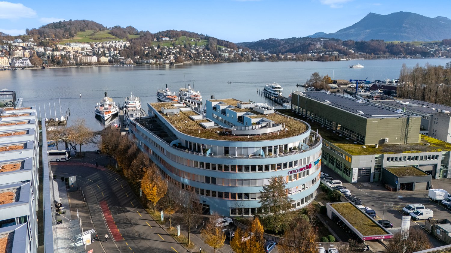 Modern building overlooking a lake with boats docked, surrounded by urban environment