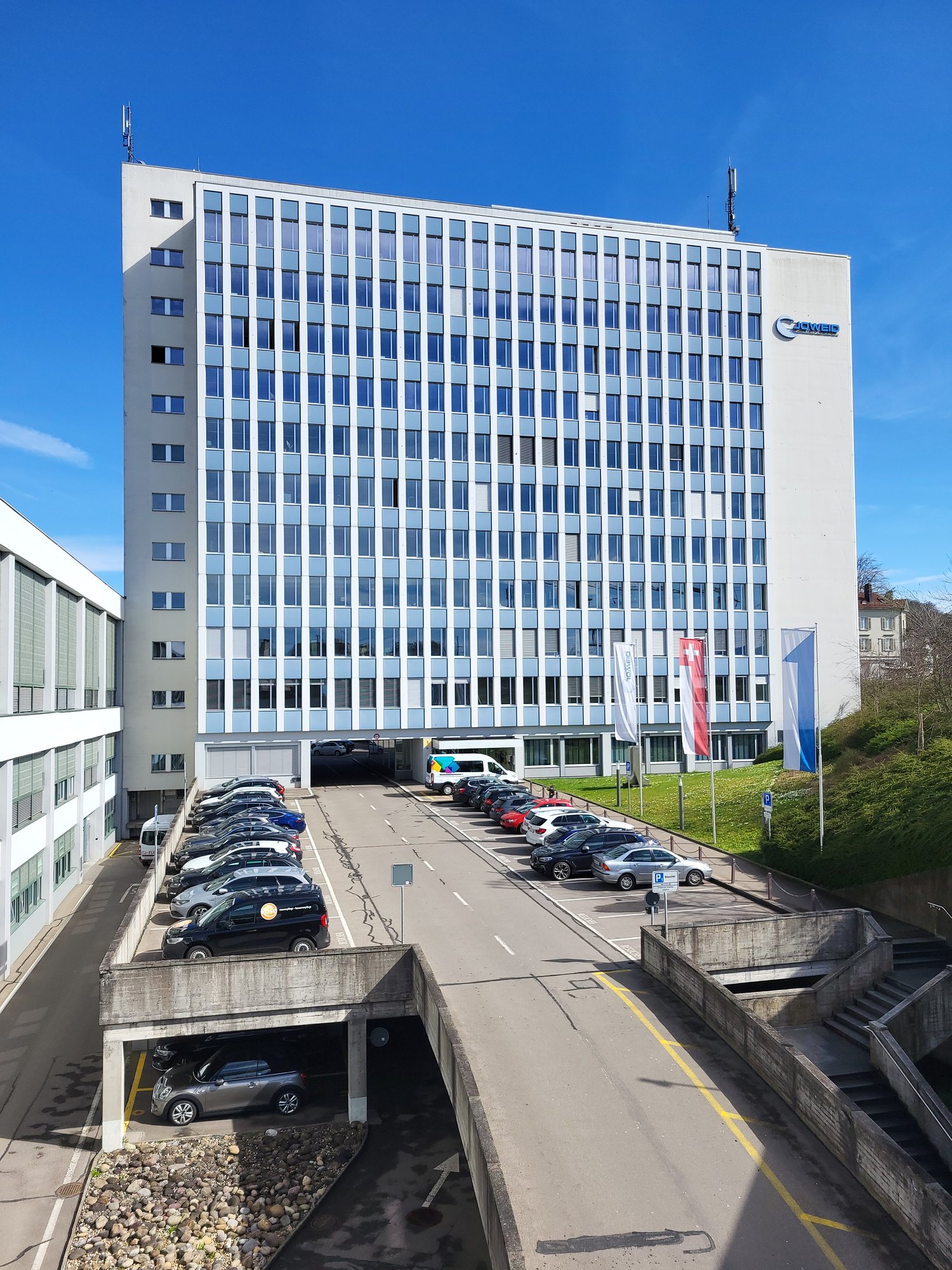 White building, glass windows, many floors, parking lot in front, street view