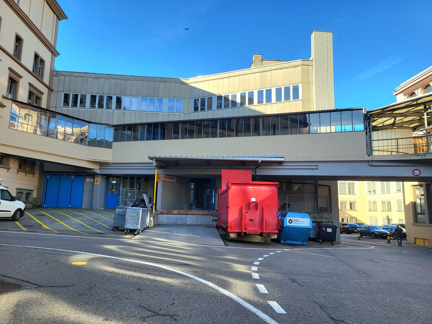 modern building with glass walls, raised ground floor,  blue entrance doors, cars parked in front