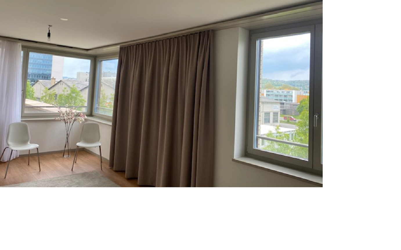 a room with a large window overlooking a city skyline, brown curtains, and two white chairs