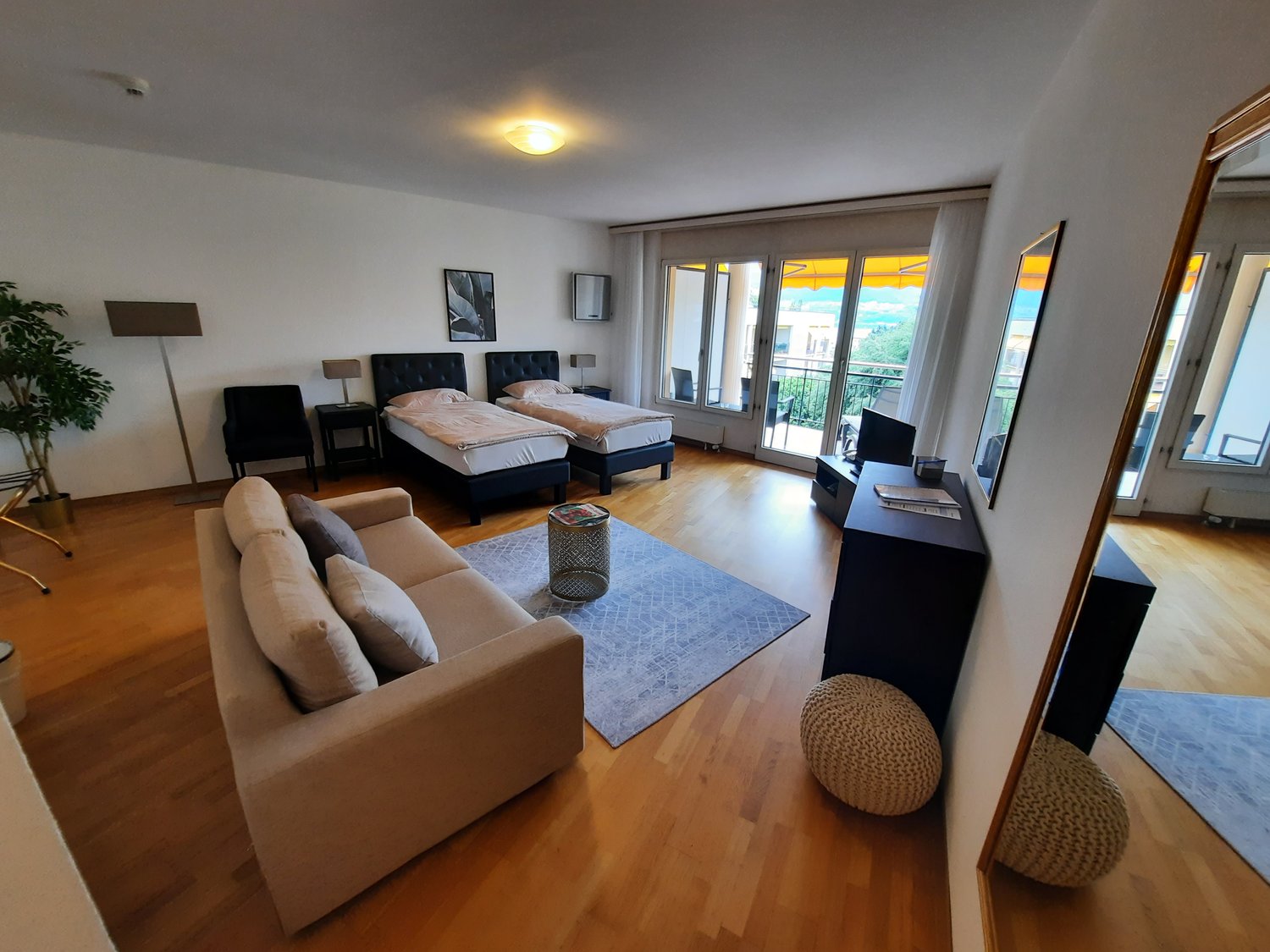 Two twin beds, couch, side tables, TV, lamps, rug, large windows, balcony with chairs