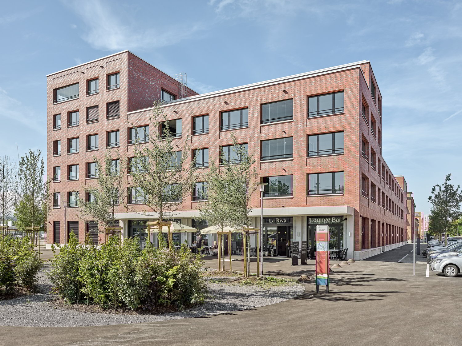 Multi-story brick building with large windows, balconies, and ground-floor commercial spaces including a lounge bar and cafe.
