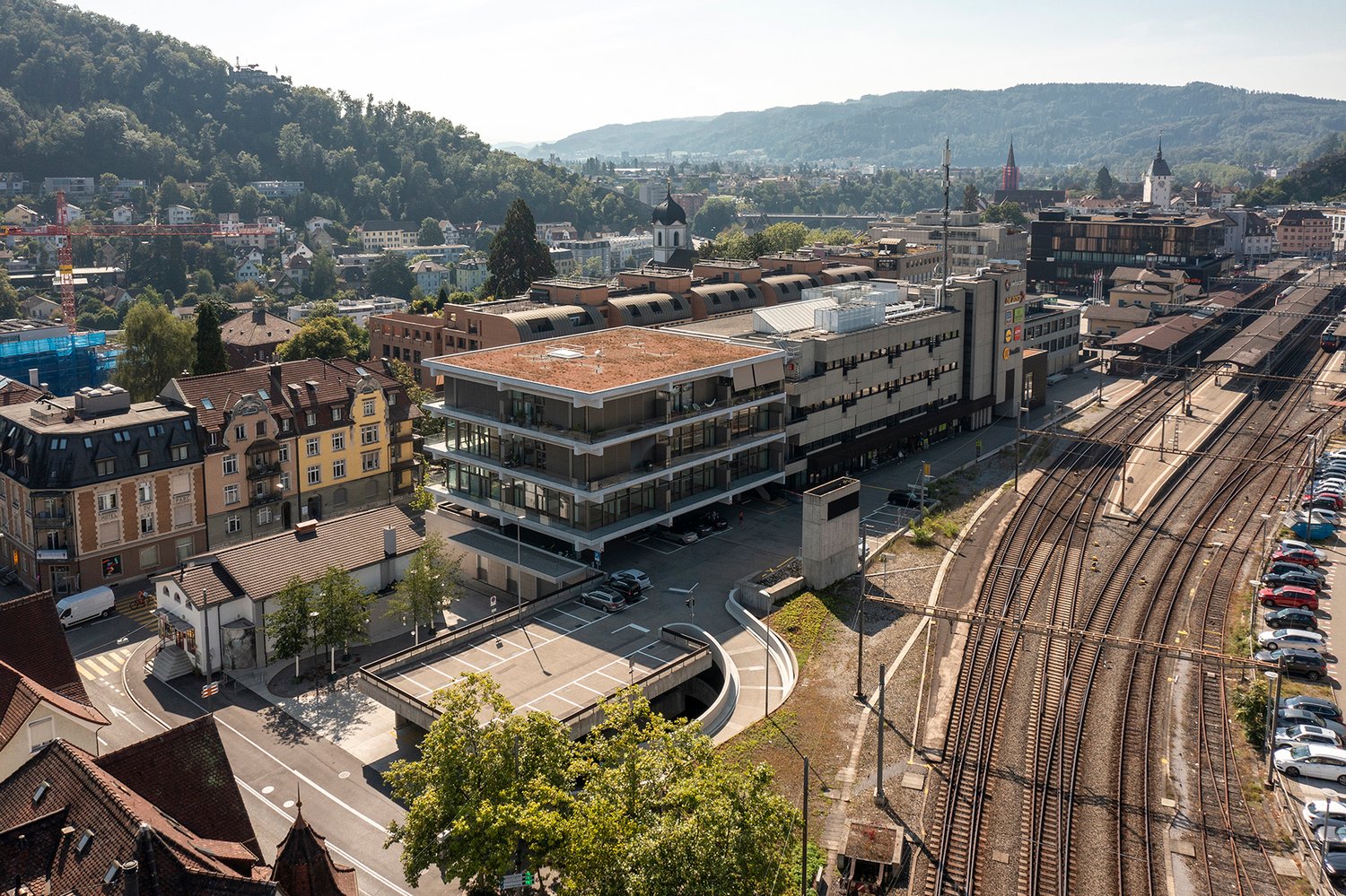 Building with multiple stories, green roof, glass windows, parking lot, train tracks